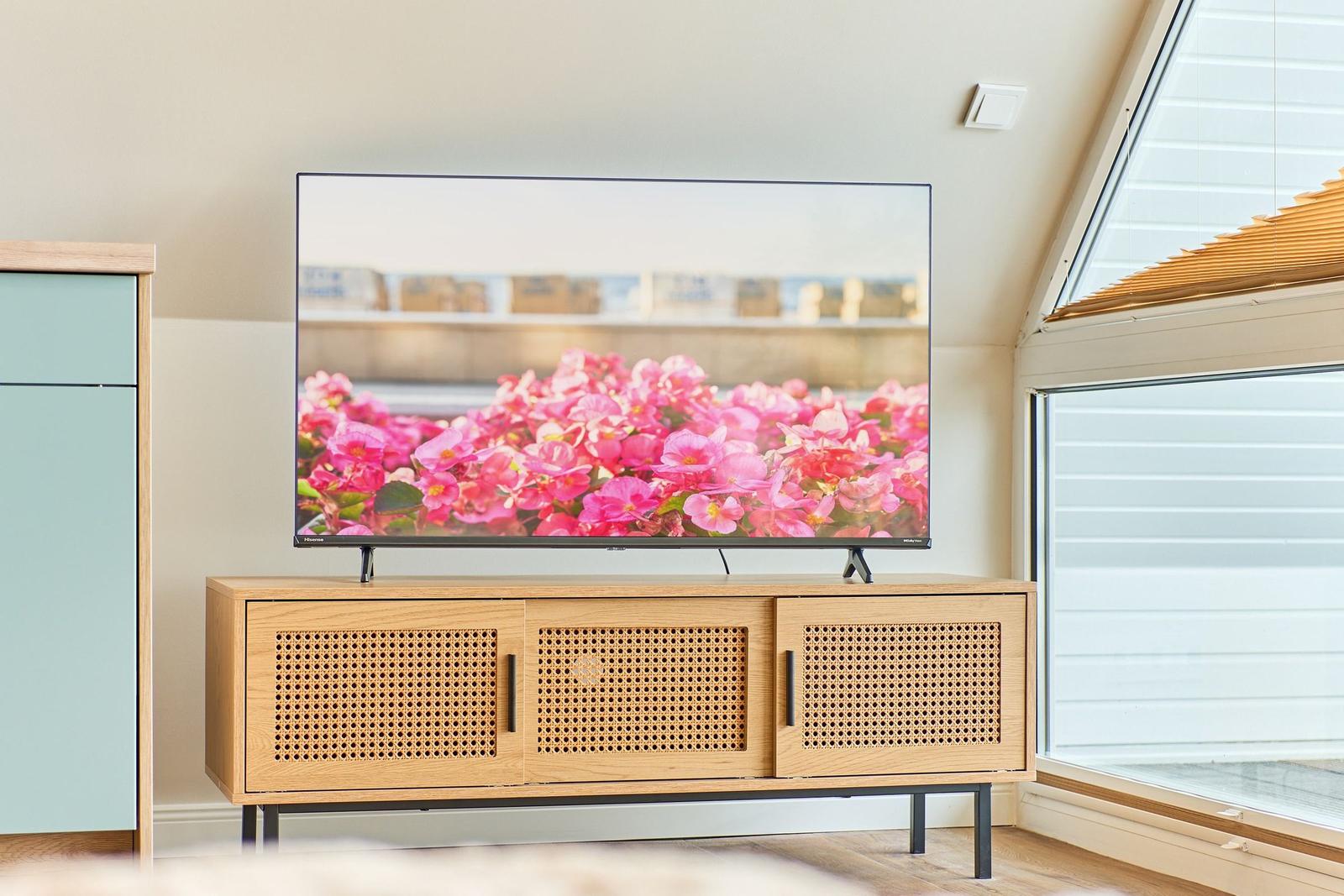 TV auf Holzboard mit Körbchenfronten, daneben Fenster mit Jalousie.