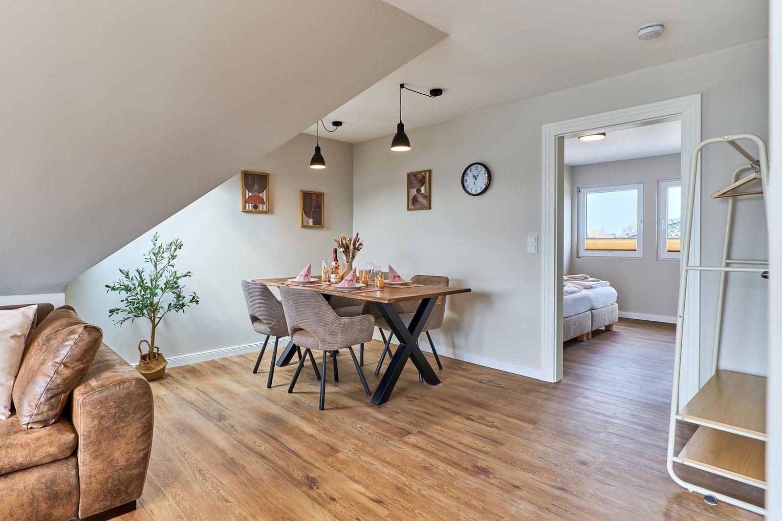Wohn- und Essbereich mit Sofa, Tisch und Stühlen. Durchgang zur Schlafzimmer.