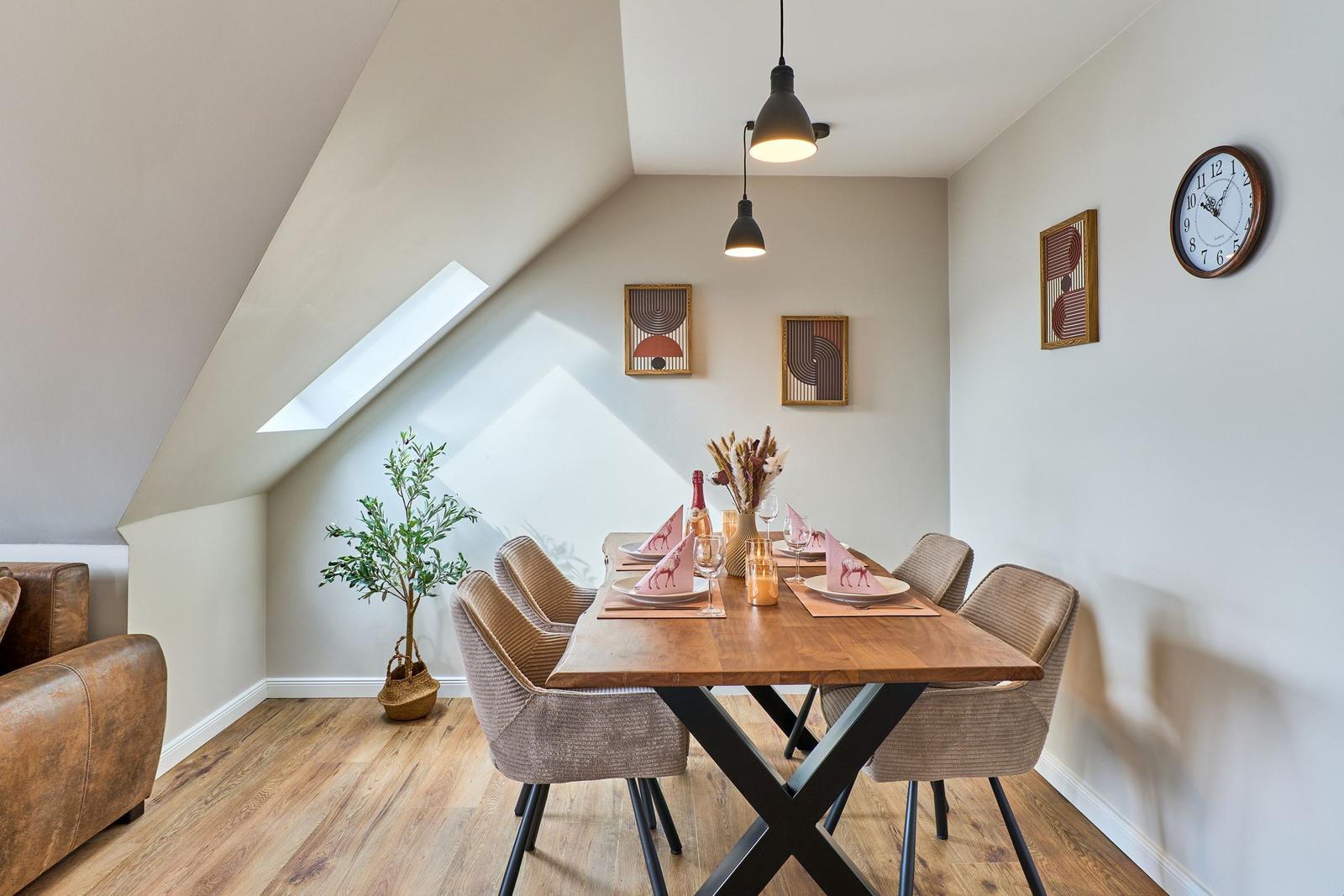 Esszimmer mit Holztisch, Stühlen und Dachfenster. Wanduhr und Bilder an der Wand.
