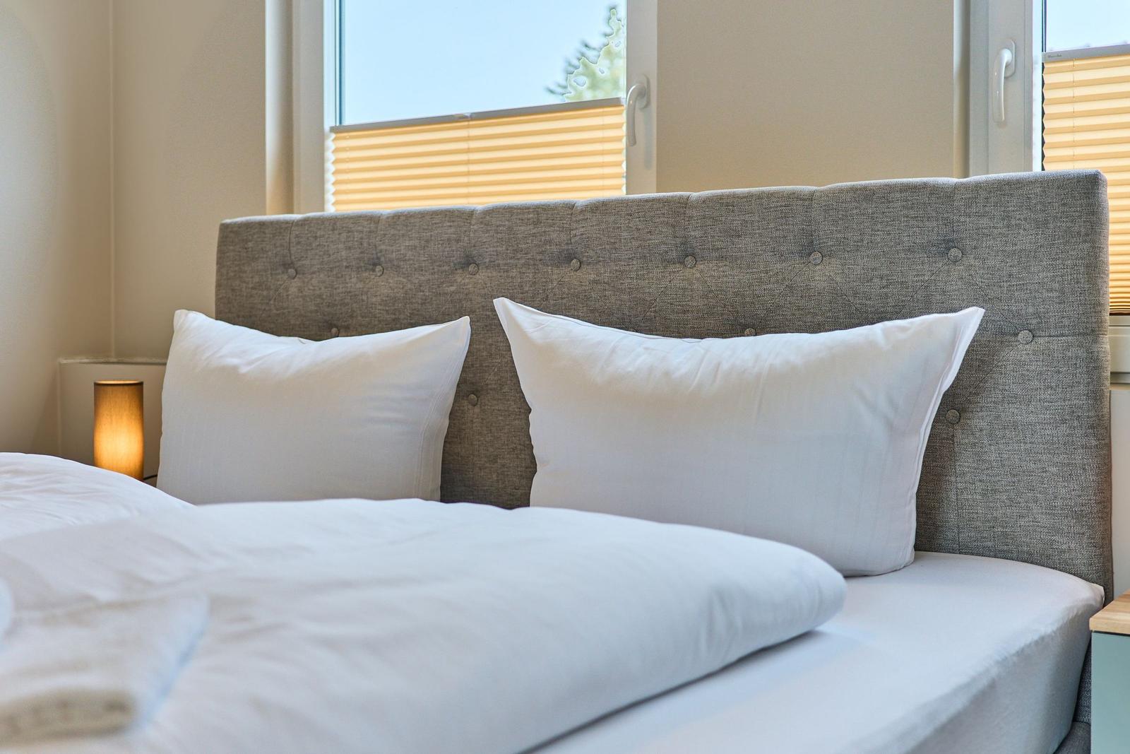 Ein Bett mit weißer Bettwäsche und Kissen vor einem Fenster mit Jalousie.