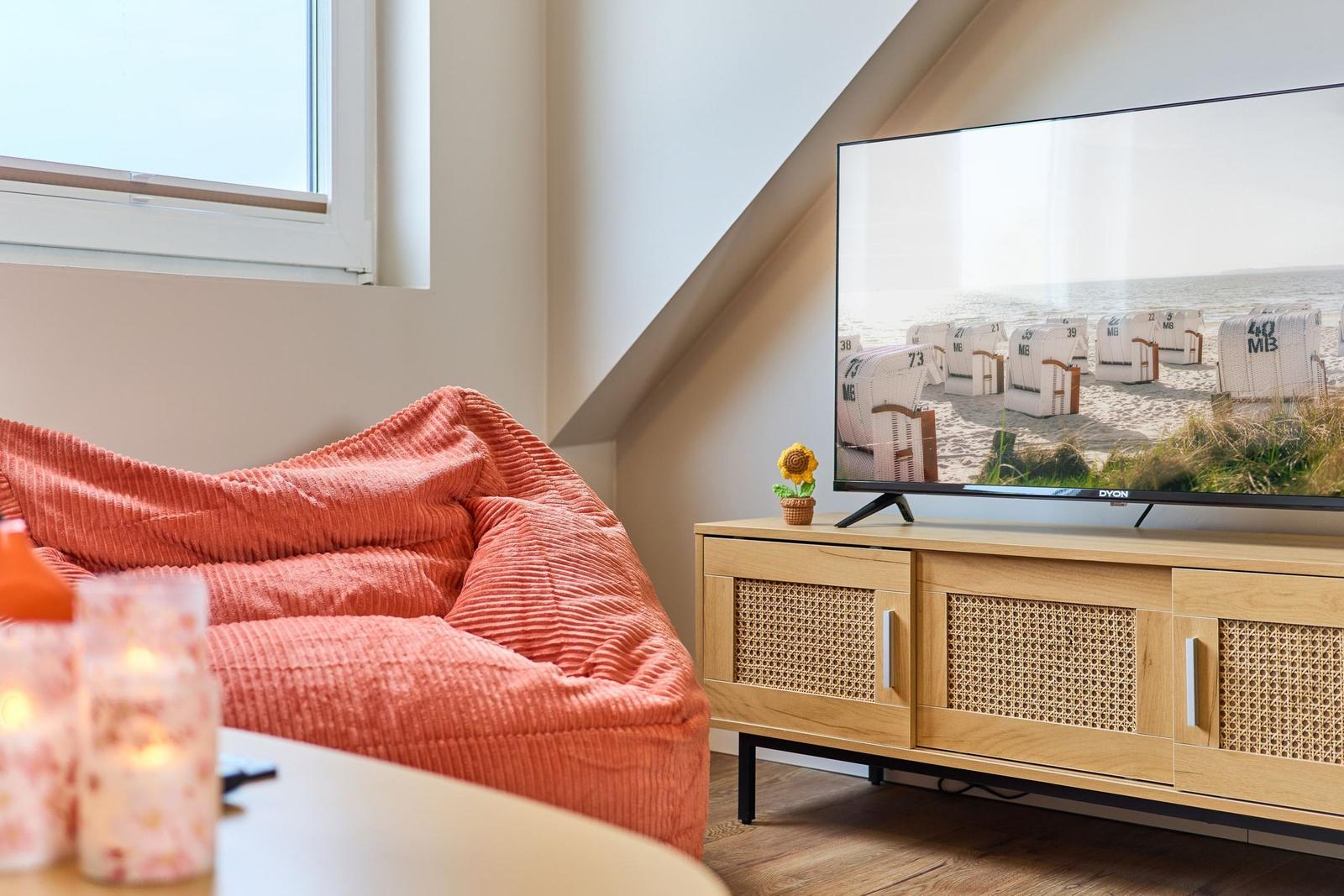 Ein Wohnzimmer mit einem orangefarbenen Sitzkissen, einem Fernseher und einem Holzschrank.