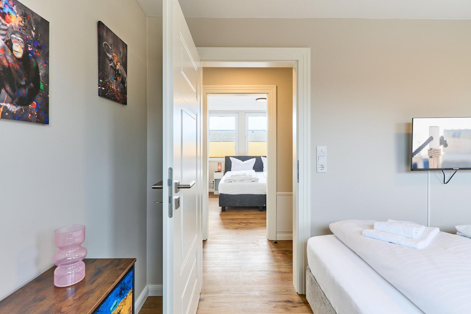 Zimmer mit Bett, Fernseher und Kunst an der Wand. Durchgang zu weiterem Schlafzimmer.