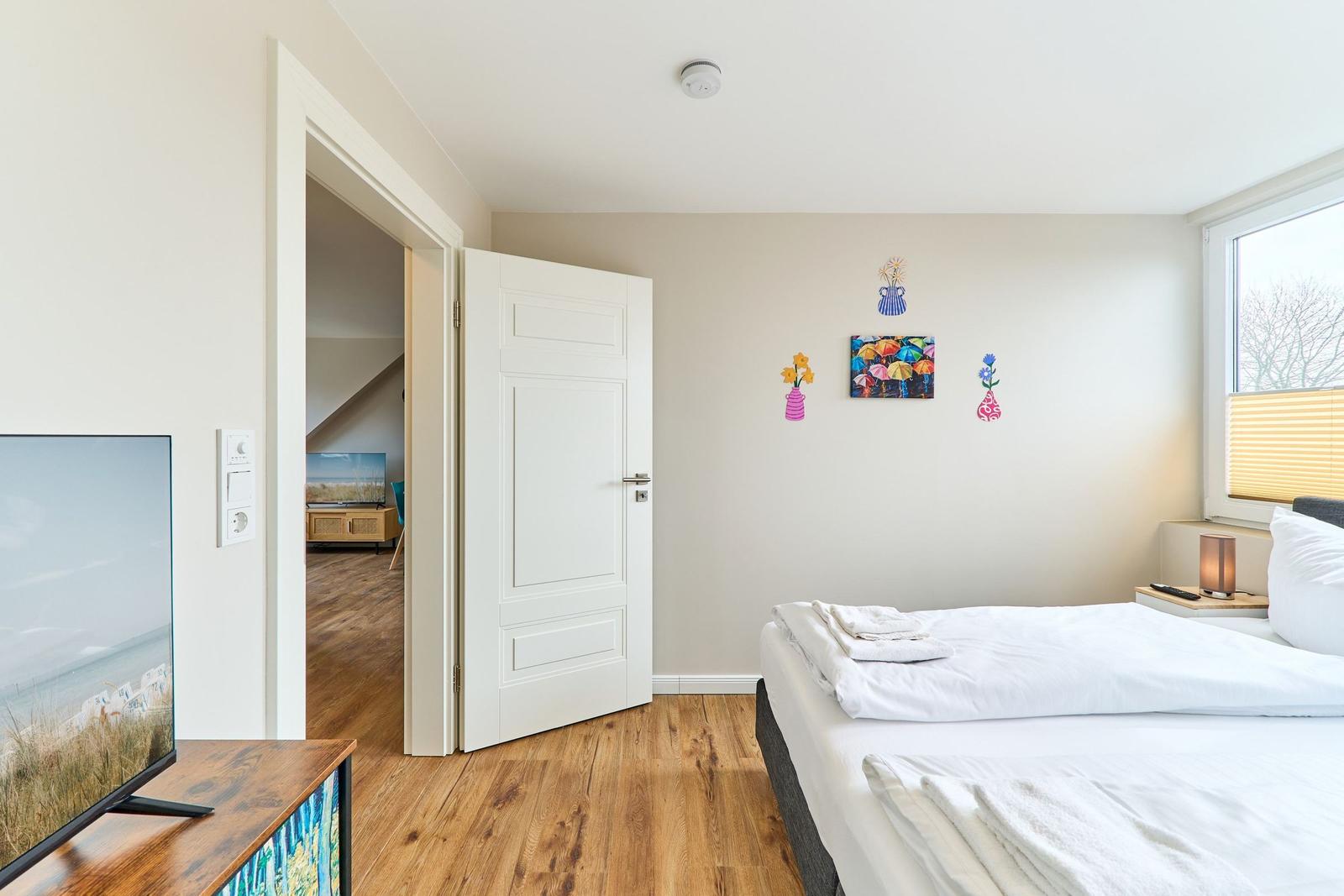 Schlafzimmer mit Bett, Fernseher und Blick in angrenzenden Raum.