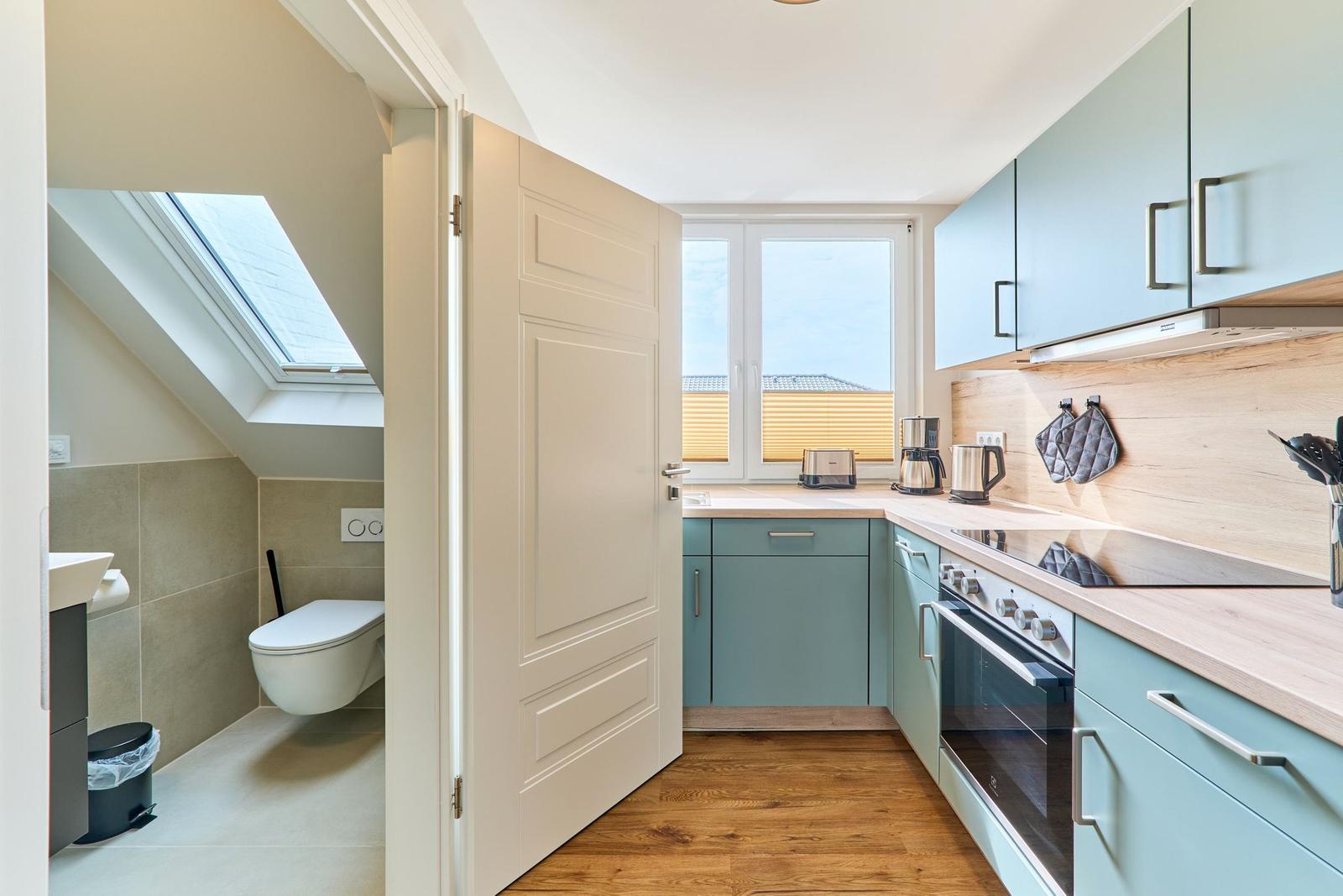 Küche mit hellblauen Schränken und Holzboden. Nebenraum mit Toilette und Dachfenster.