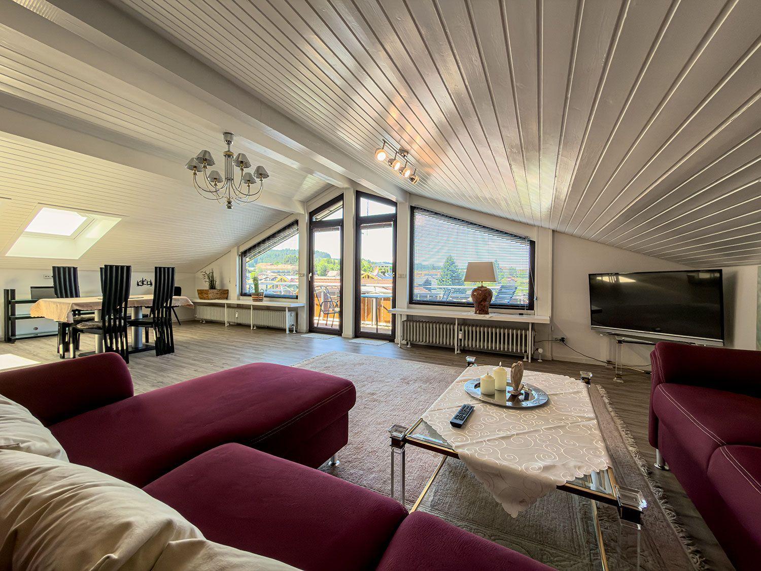 Living and dining area with red sofa, TV, and view of balcony.