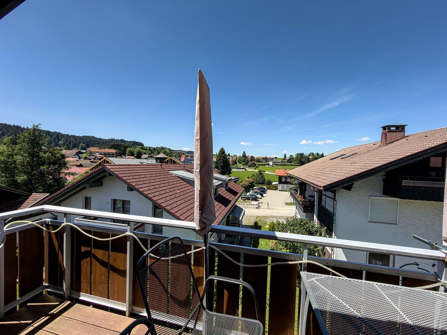 Balcony with seating and view of rooftops and green areas.