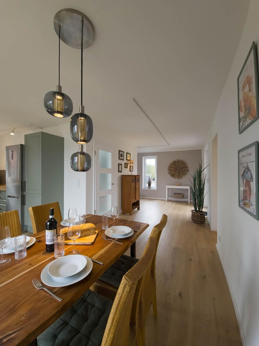 Esszimmer mit Holztisch, Stühlen und Hängelampen. Im Hintergrund Küche und Wohnbereich.