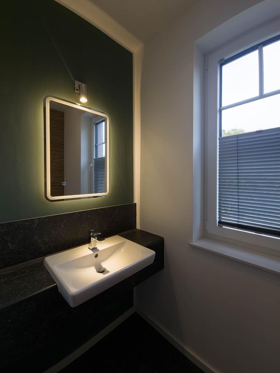 Waschbecken mit beleuchtetem Spiegel und Fenster mit Jalousie.