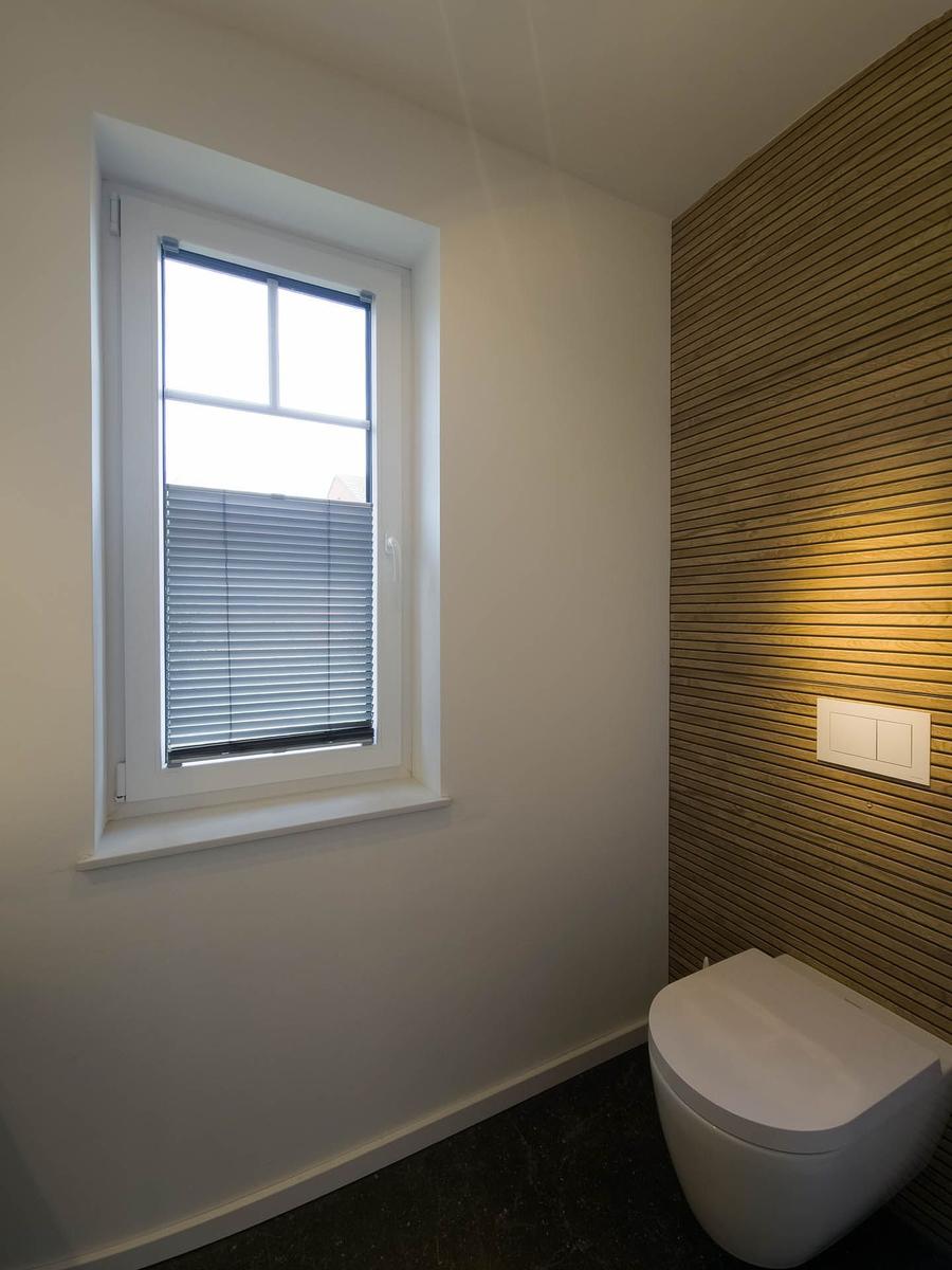 Bad mit Toilette, Holzwand und Fenster mit Jalousie.