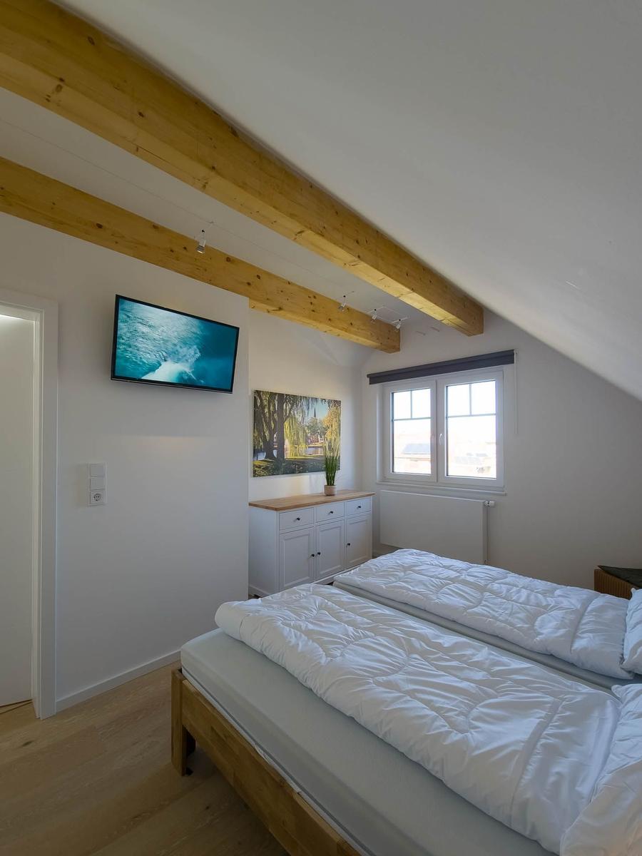 Schlafzimmer mit Doppelbett, Holzbalken und TV an der Wand.