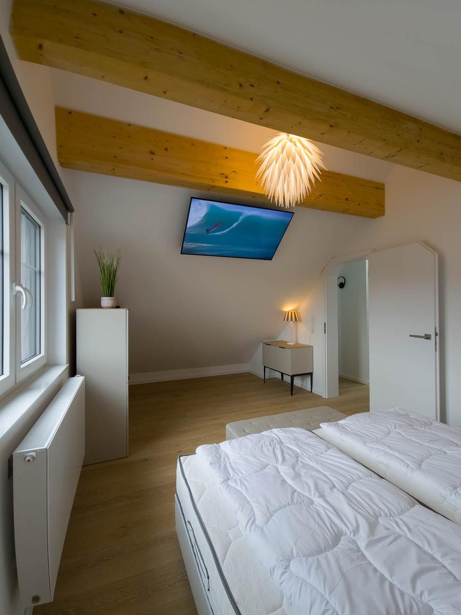 Schlafzimmer mit Doppelbett, Fernseher und Holzbalken an der Decke.