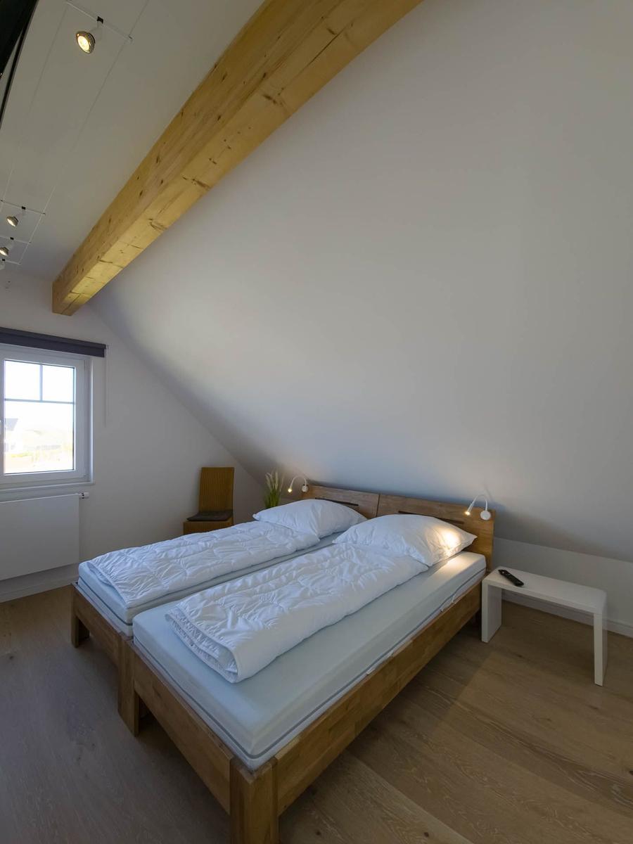 Schlafzimmer mit Doppelbett, Holzboden und Holzbalken an der Decke.
