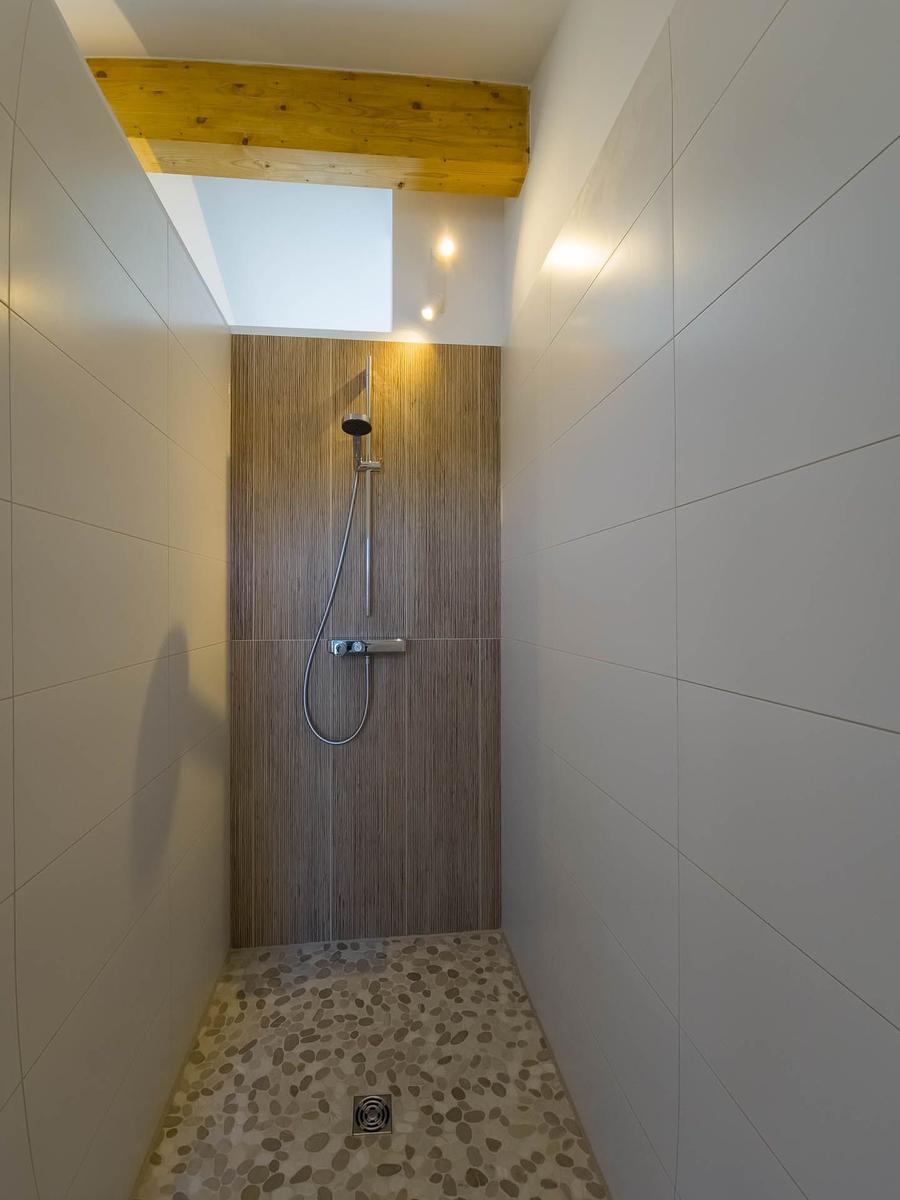 Dusche mit Holzverkleidung, Boden aus Kieselsteinen und Dachfenster.