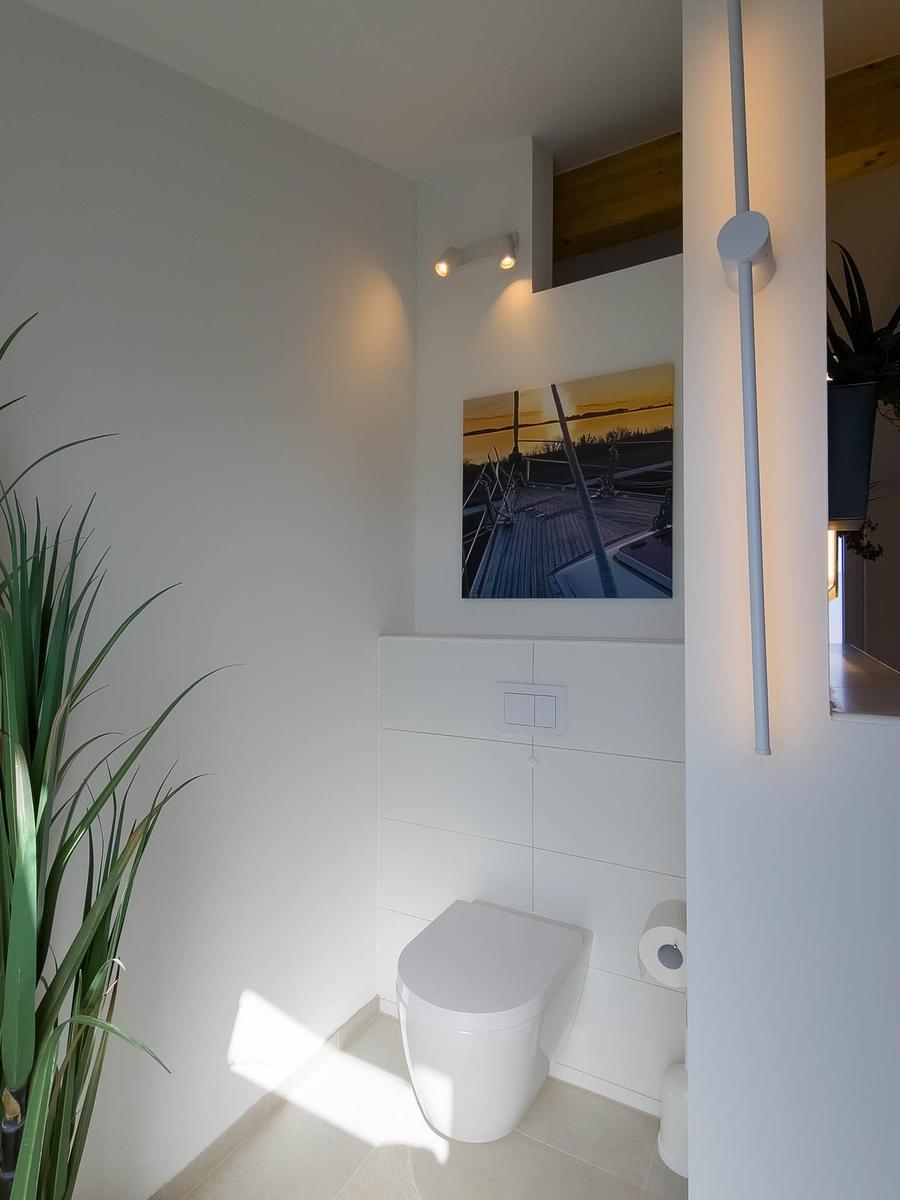 Toilettenbereich mit Wandbild, Pflanze und moderner Beleuchtung.