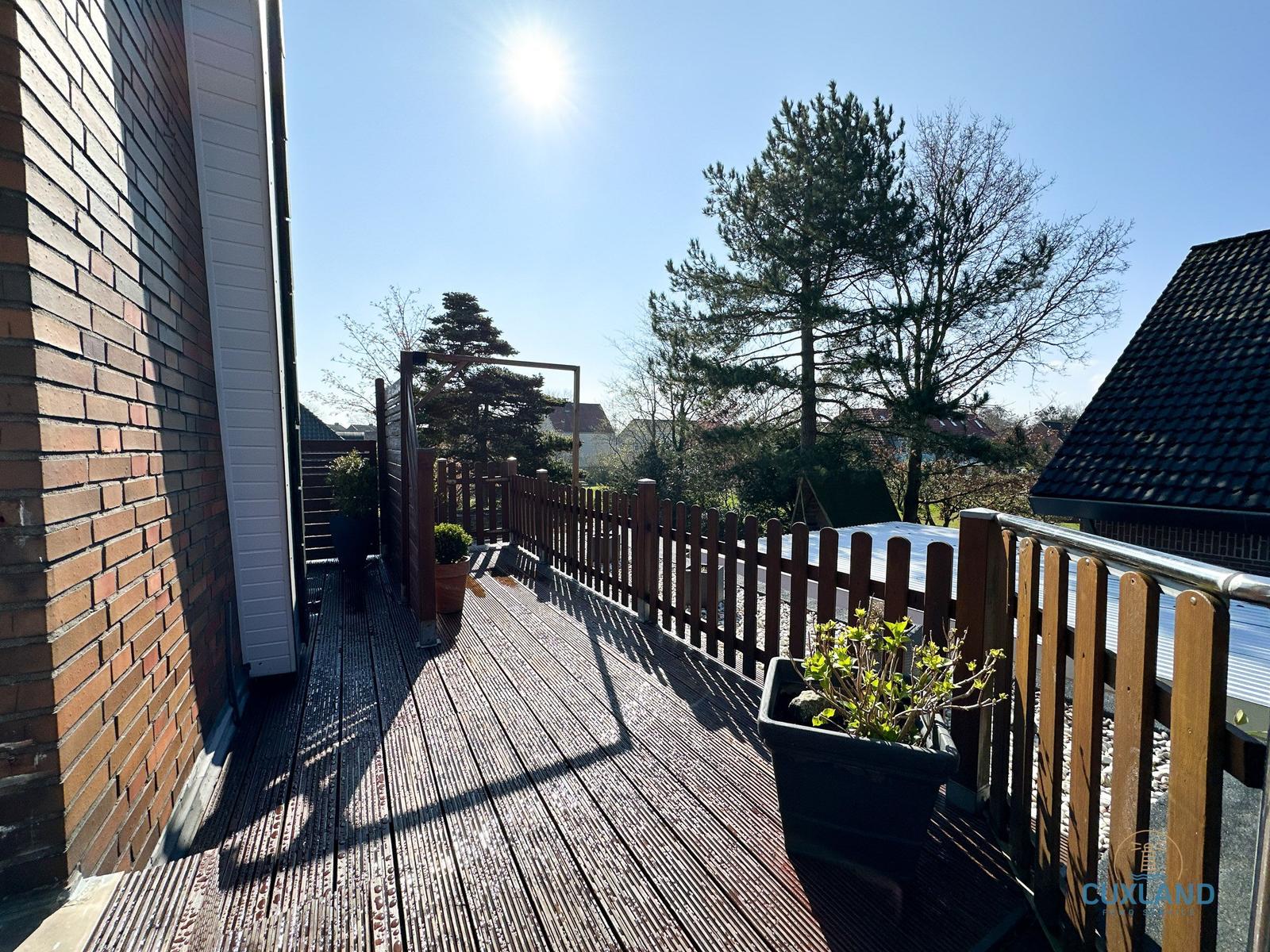 Holzterrasse mit Pflanzen und Blick auf Bäume und Nachbarhäuser.
