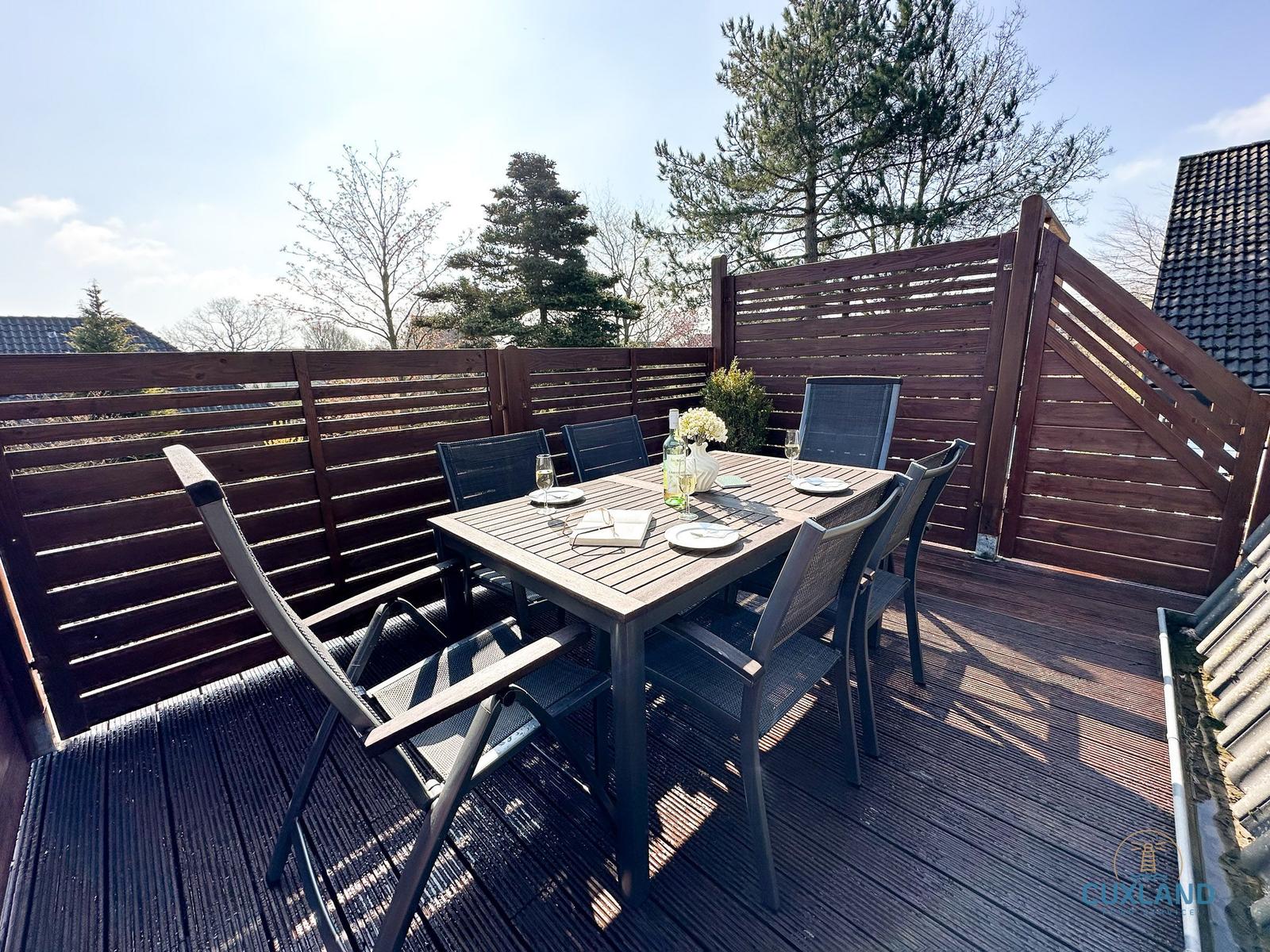 Terrasse mit Holzgeländer, Tisch und sechs Stühlen für gemütliche Mahlzeiten im Freien.