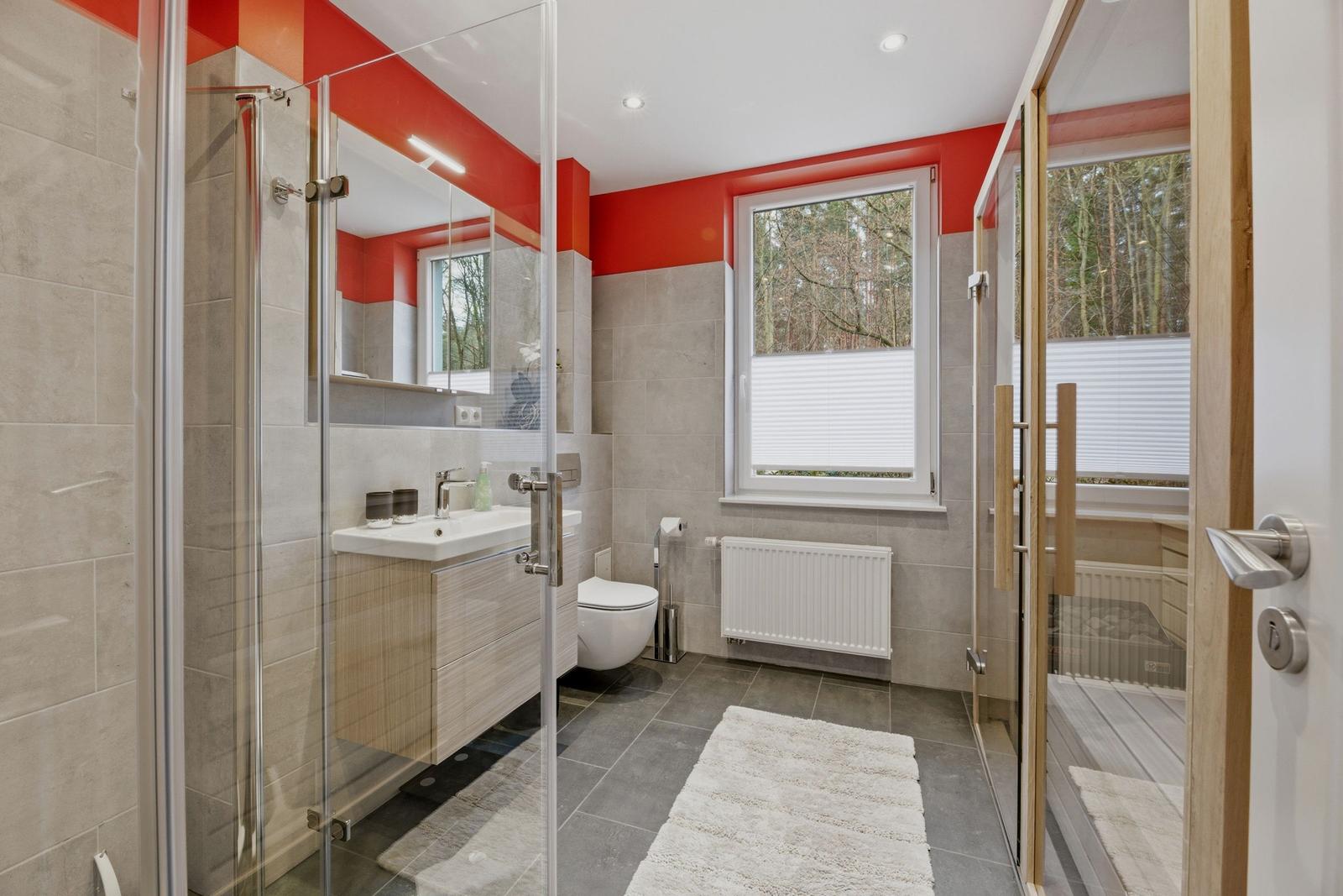 Badezimmer mit Dusche, Toilette und Fenster zur Waldsicht.