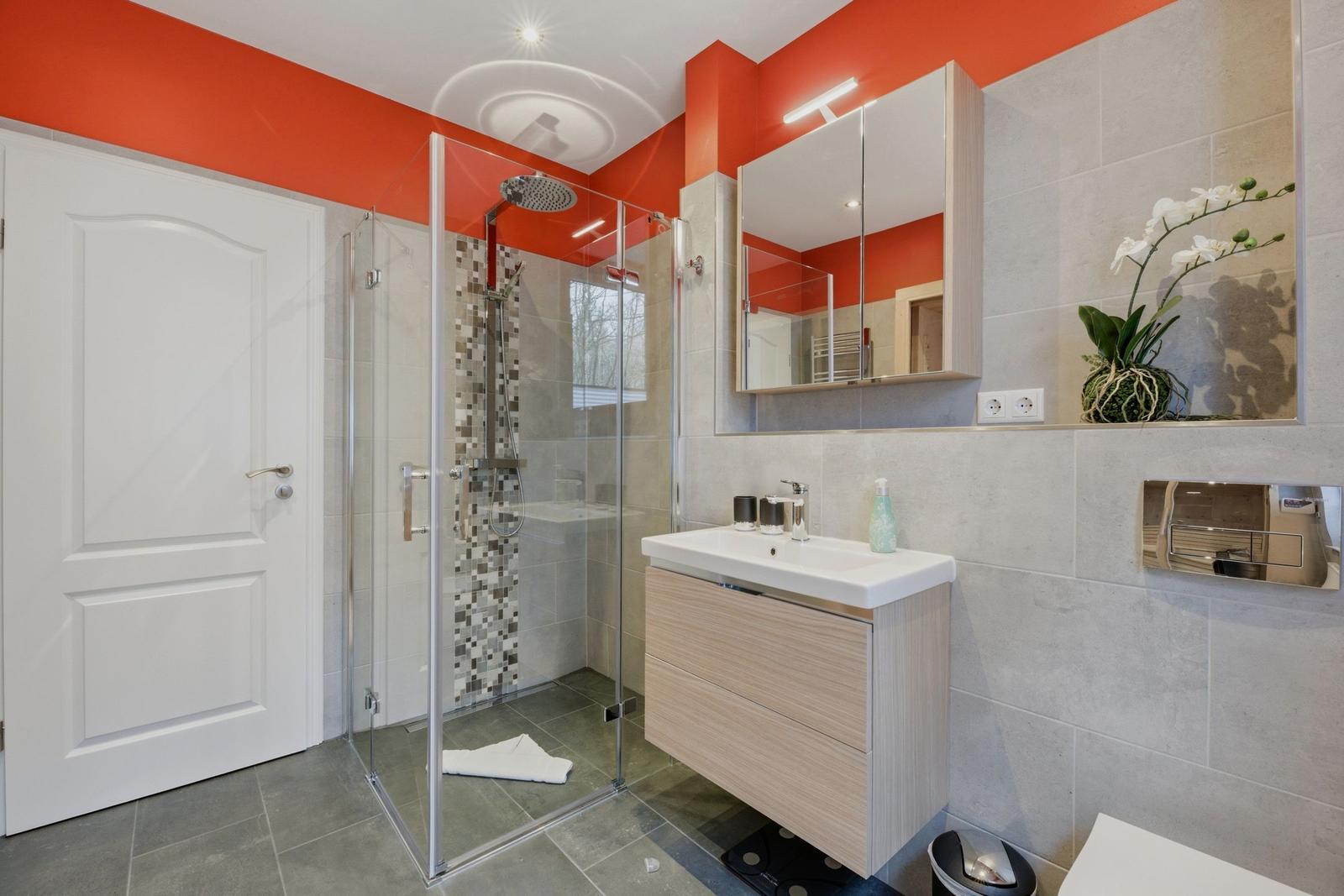Badezimmer mit Dusche, Waschbecken und Spiegel.