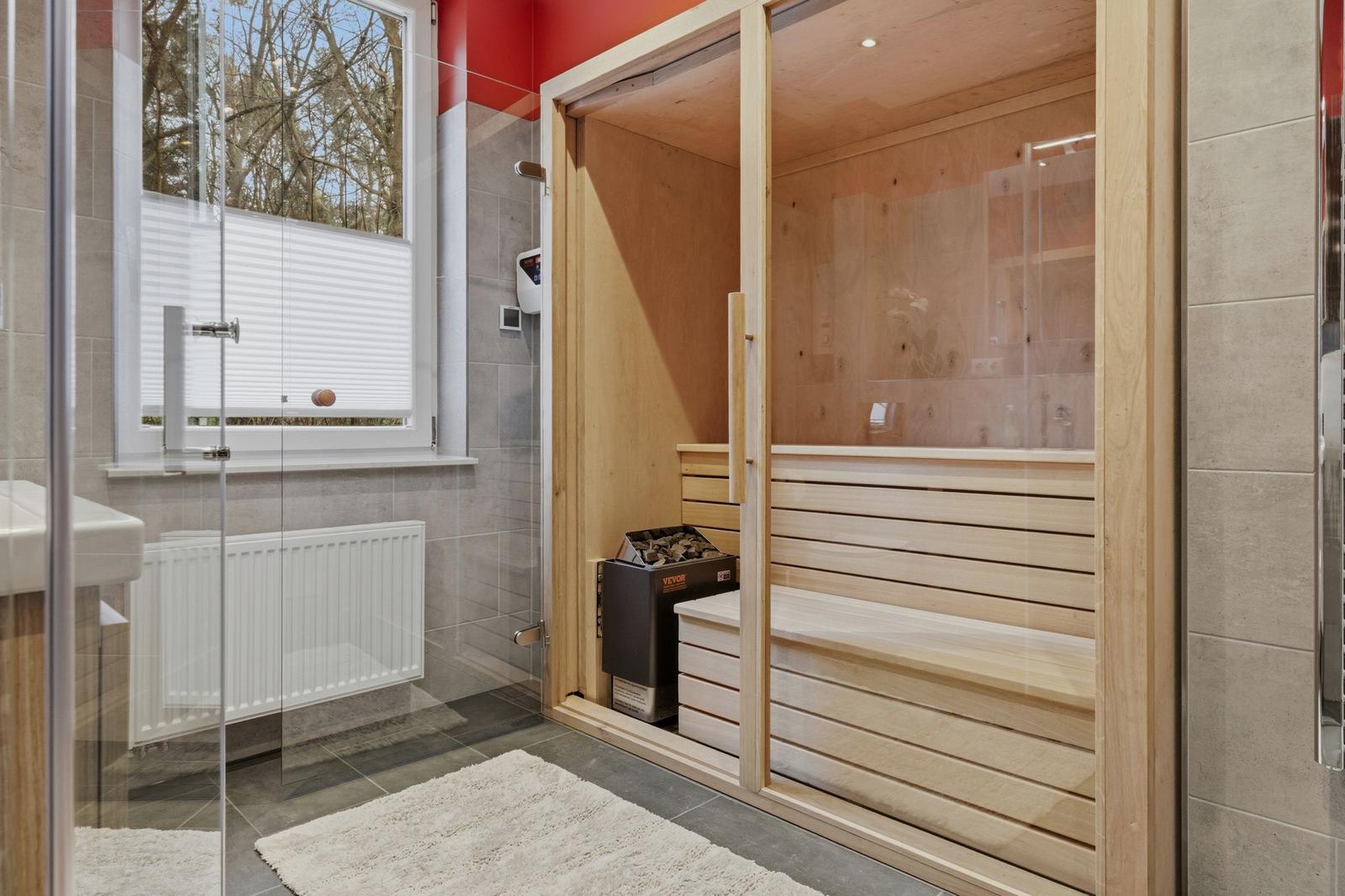 Sauna mit Holzbank und Glaswand. Fenster mit Jalousie. Fliesenboden und Heizung.