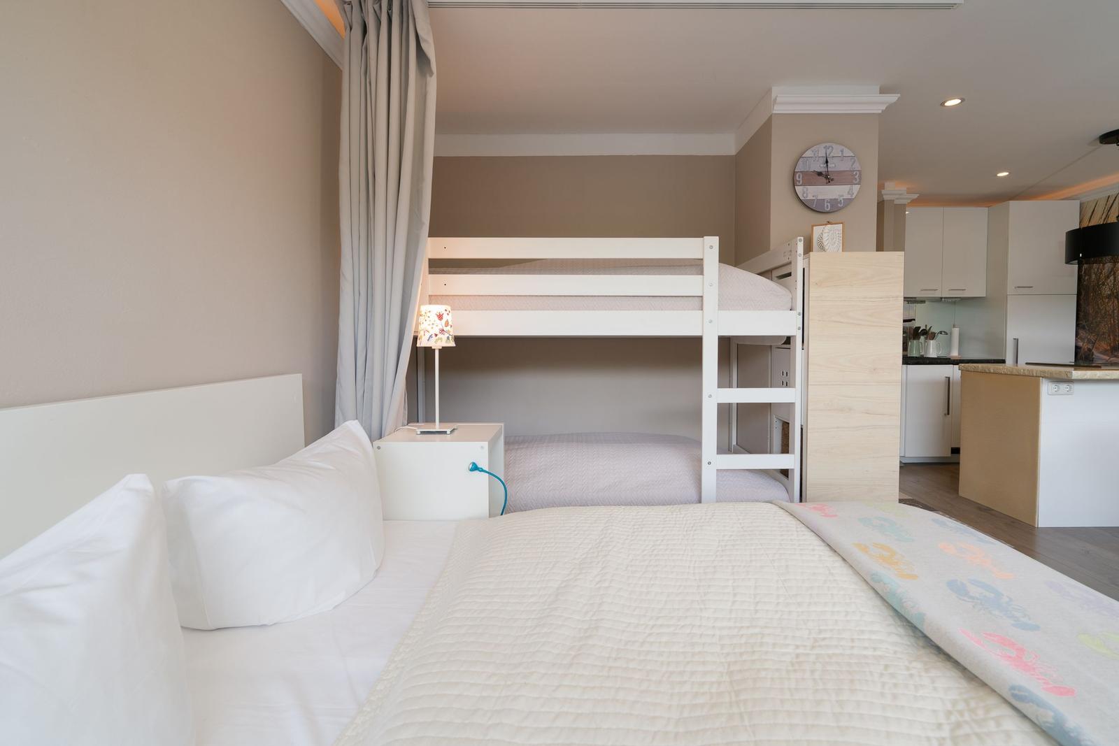 Zimmer mit Doppelbett und Schlafcouch, daneben Doppelstockbett mit Nachttisch und Lampe.