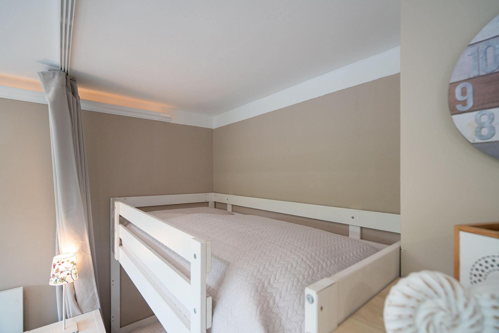 Schlafzimmer mit weißem Hochbett, beige Wände und Nachttischlampe.