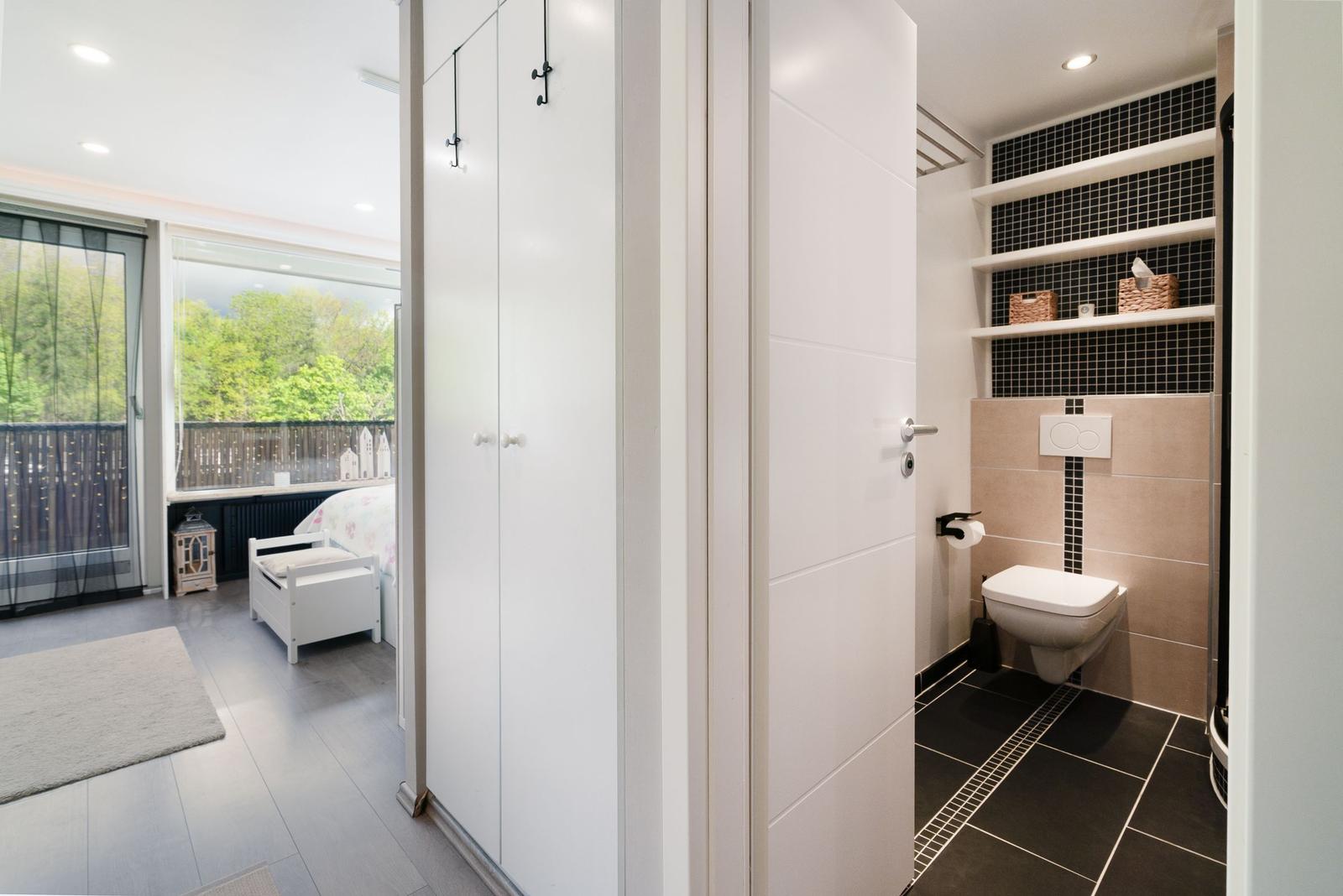 Badezimmer mit Toilette und Regalen. Nebenraum mit Bett und Balkon.