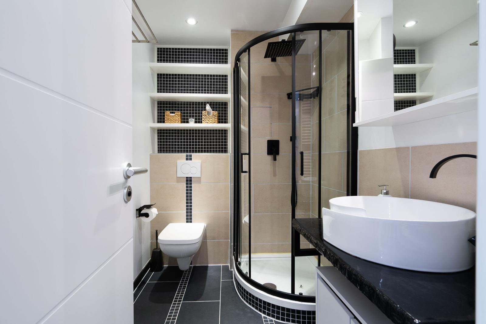 Badezimmer mit Dusche, Waschbecken und Toilette. Schwarze und weiße Fliesen.