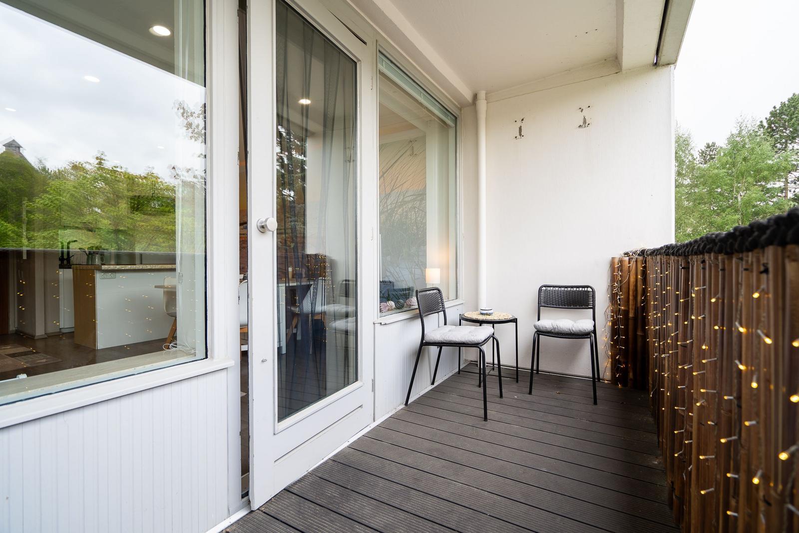 Terrasse mit zwei Stühlen und Tisch, Holzgeländer mit Lichterkette, Blick in Wohnraum.