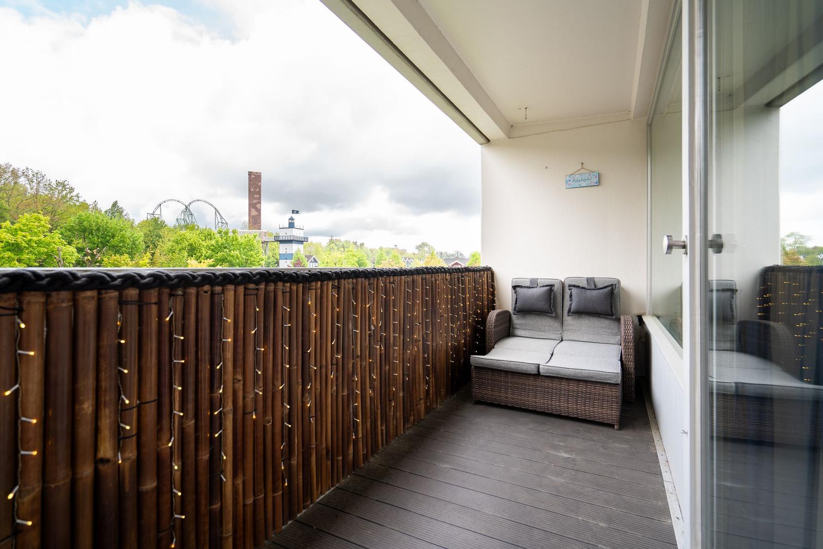 Terrasse mit Sitzbank, Holzgeländer und Lichterkette. Blick auf Wald und Sehenswürdigkeiten.