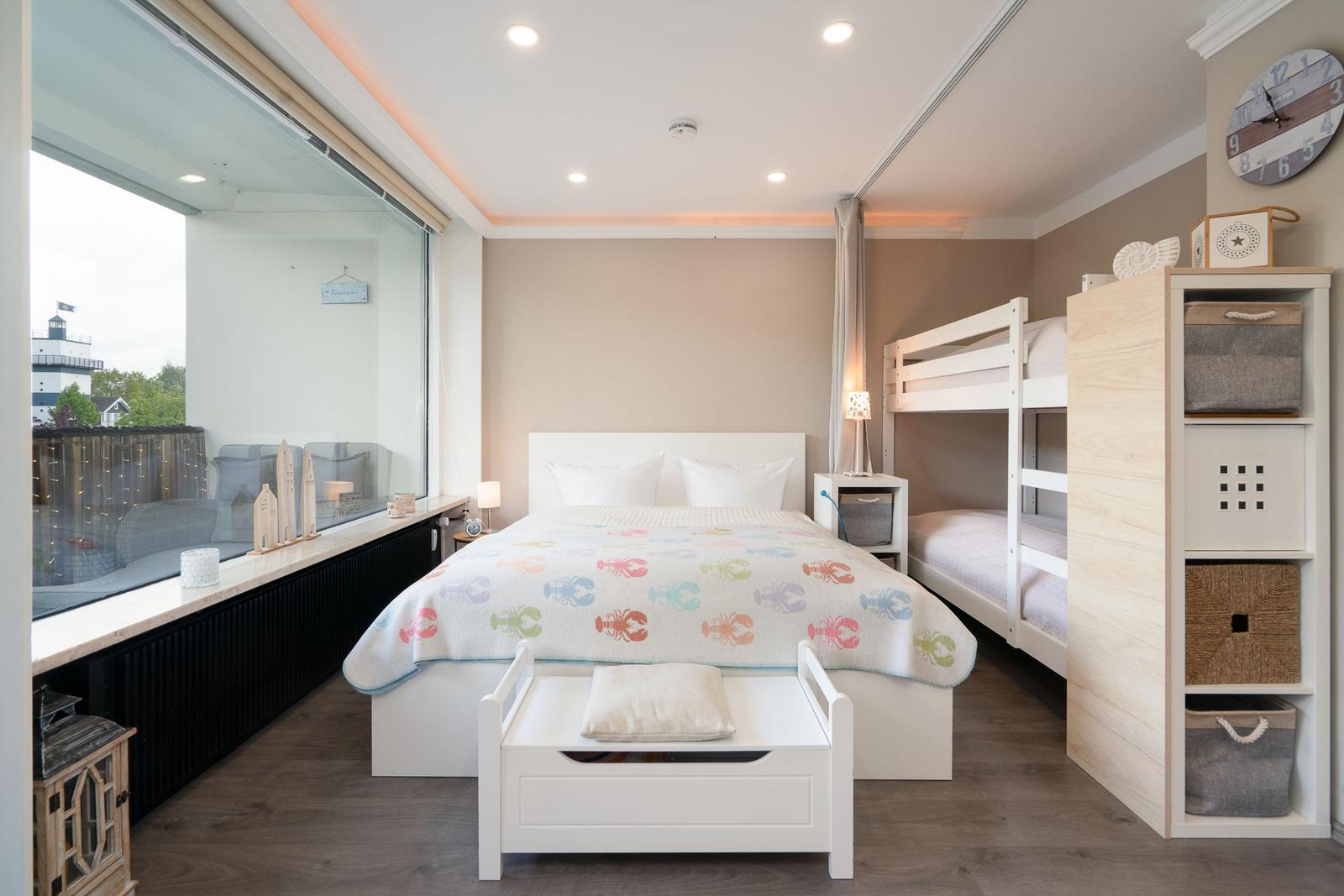 Schlafzimmer mit Doppelbett, Hochbett und großem Fenster zur Terrasse.