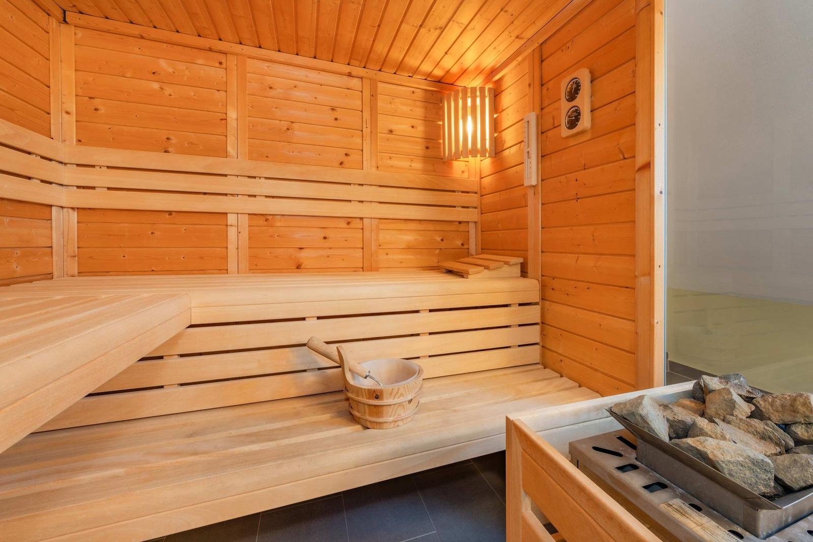 Holzsauna mit Sitzbänken, Wassereimer und Steineinsatz.