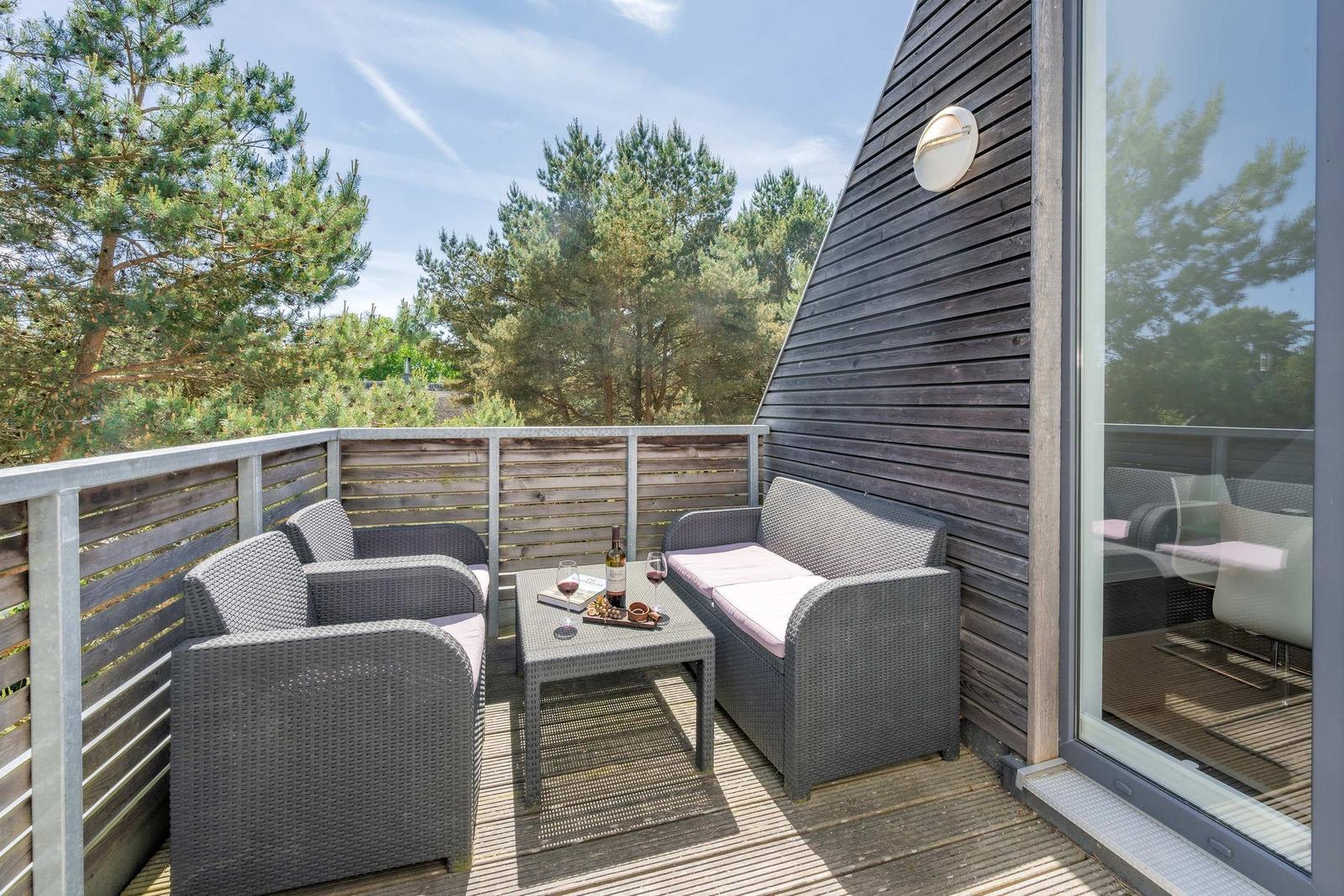 Terrasse mit Sitzgruppe, Tisch und Wein, umgeben von Bäumen und Holzwand.