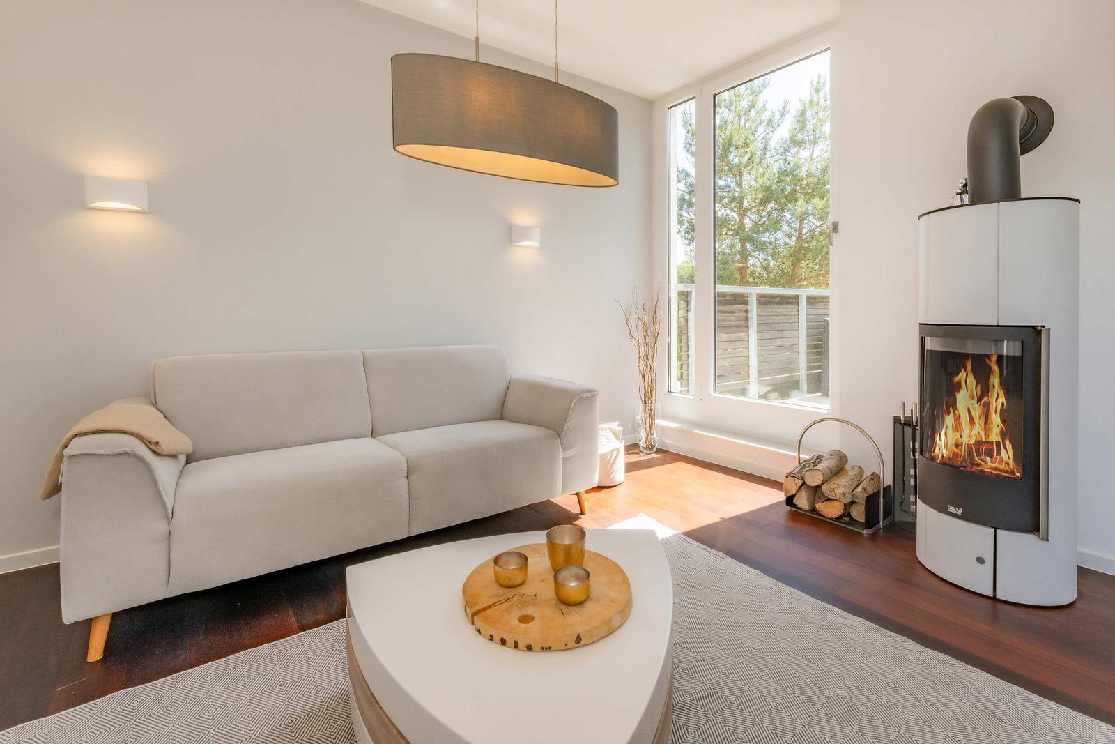 Wohnzimmer mit Sofa, Kamin und großem Fenster. Holzboden und helle Wände.