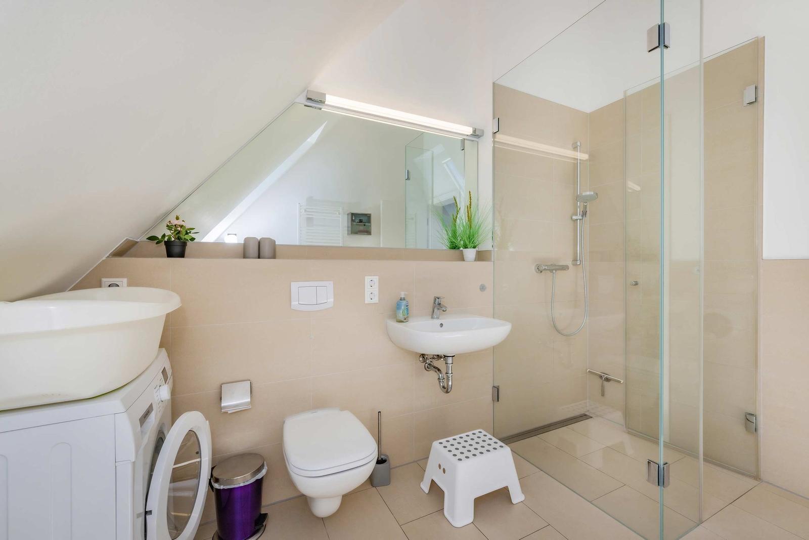 Badezimmer mit Dusche, Waschbecken, WC und Waschmaschine unter Dachschräge.