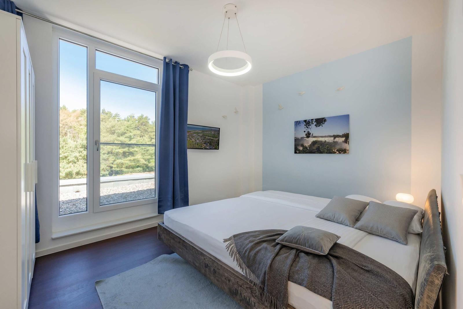 Schlafzimmer mit großem Fenster, Bett und Wandbild.