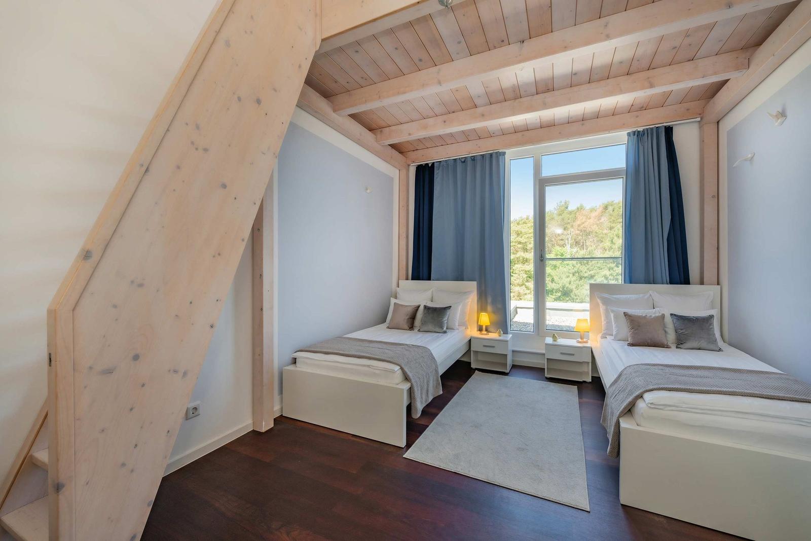 Zwei Betten mit Nachttischen und Blick auf Balkon mit Wald
