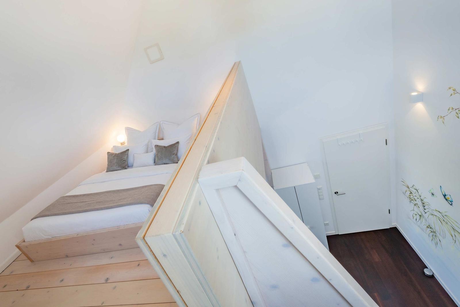 Schlafzimmer mit Dachschräge, Bett, Wandbeleuchtung und Bodenbelag.