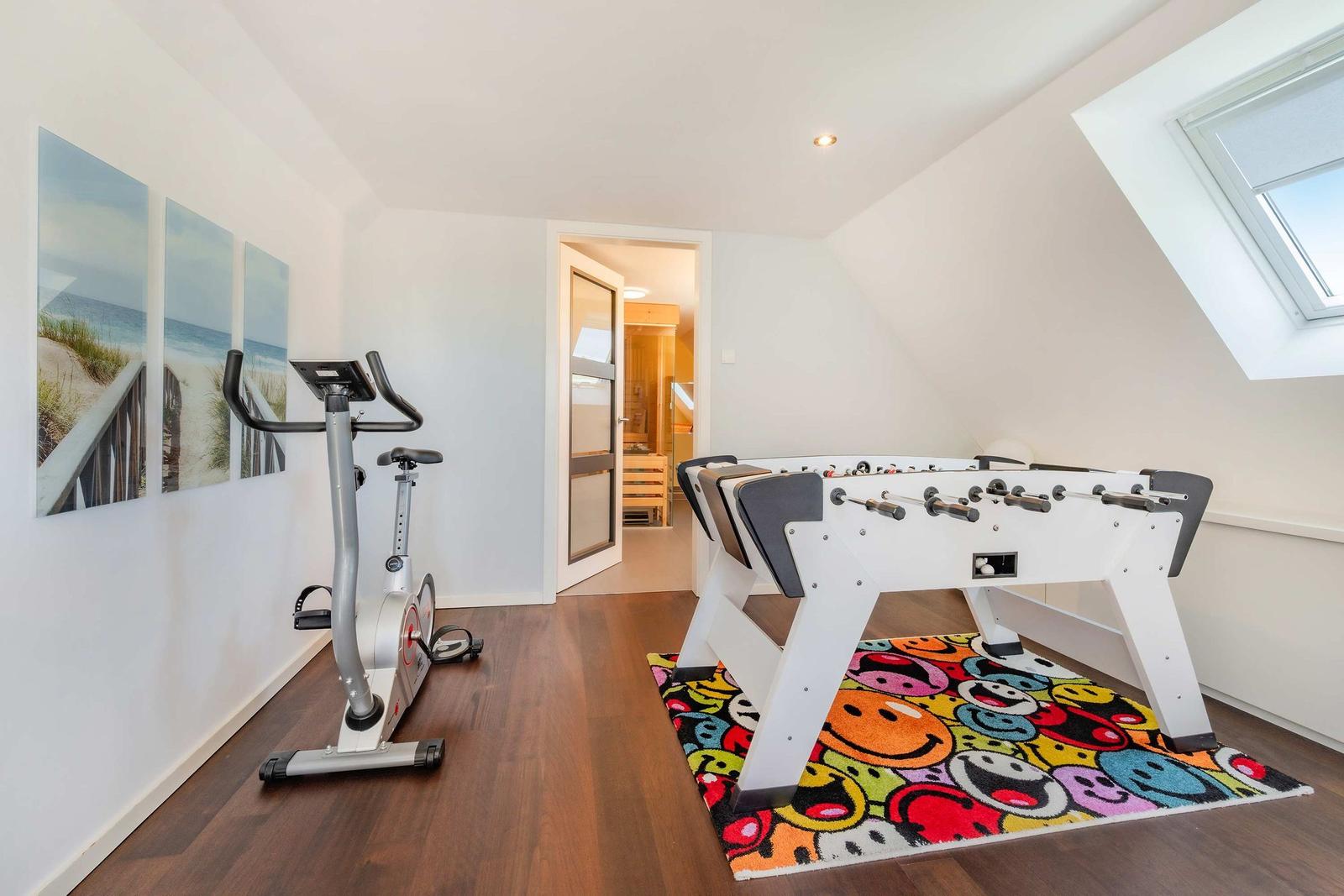 Fitnessrad und Tischfußball im Dachgeschoss mit Holzboden und Dachfenster.