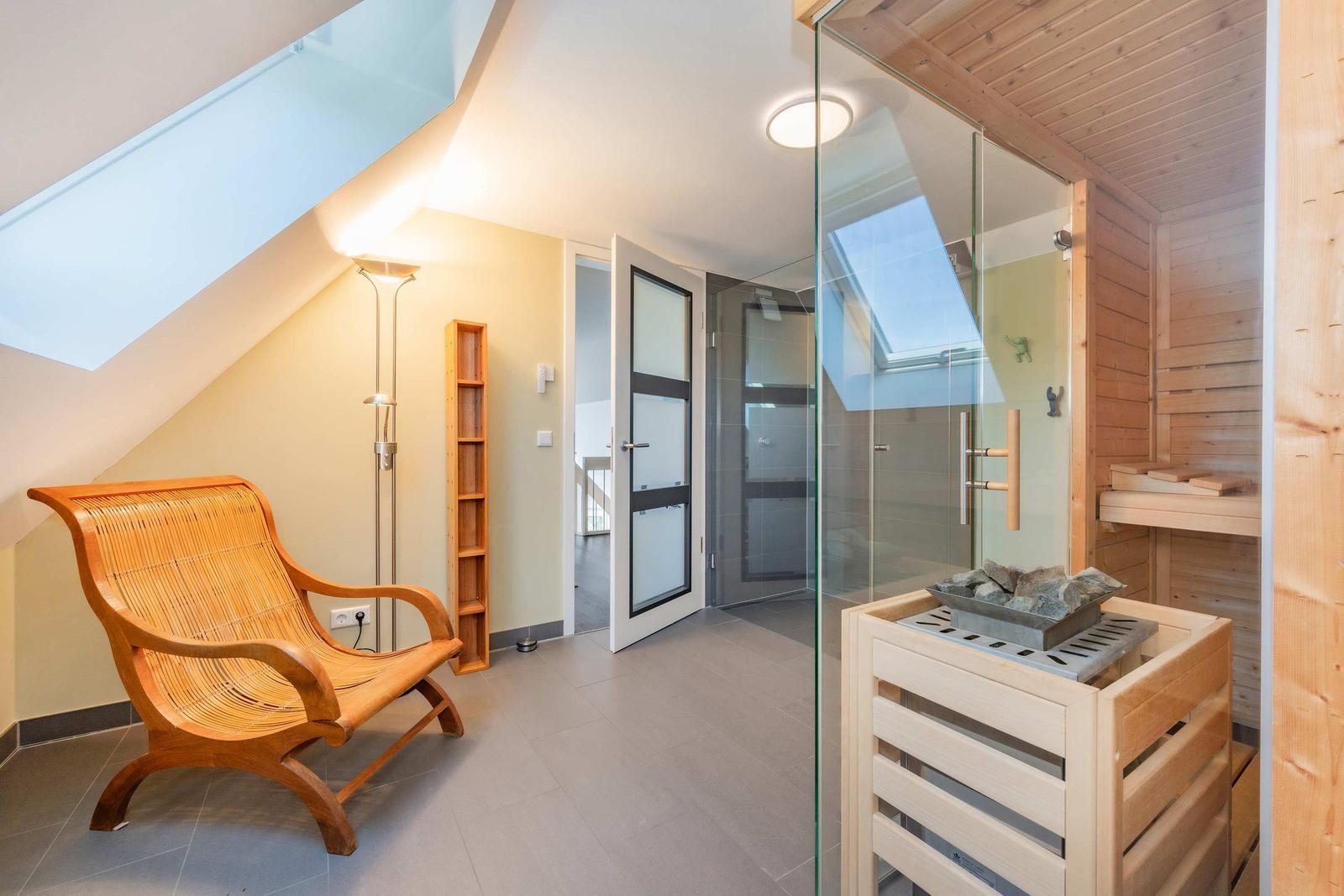 Sauna mit Glaswand und Holzbank. Links steht ein Holzstuhl unter Dachschrägen.