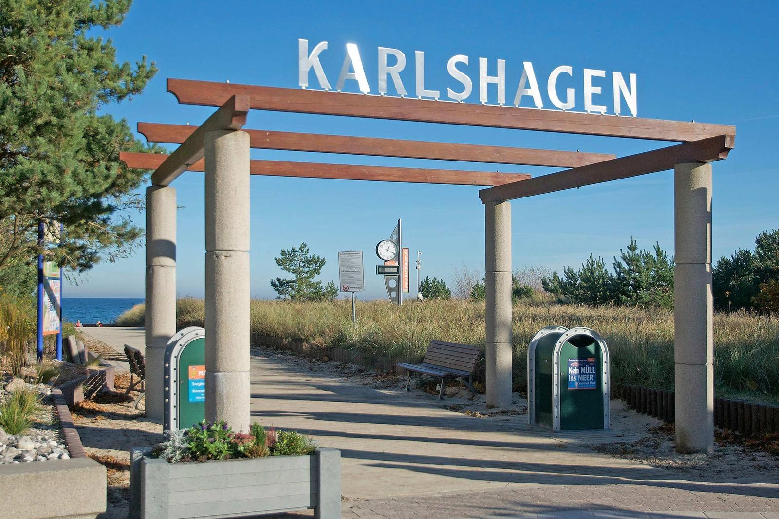Eingangsbereich von Karlshagen mit Schild, Bänken und Meerblick.