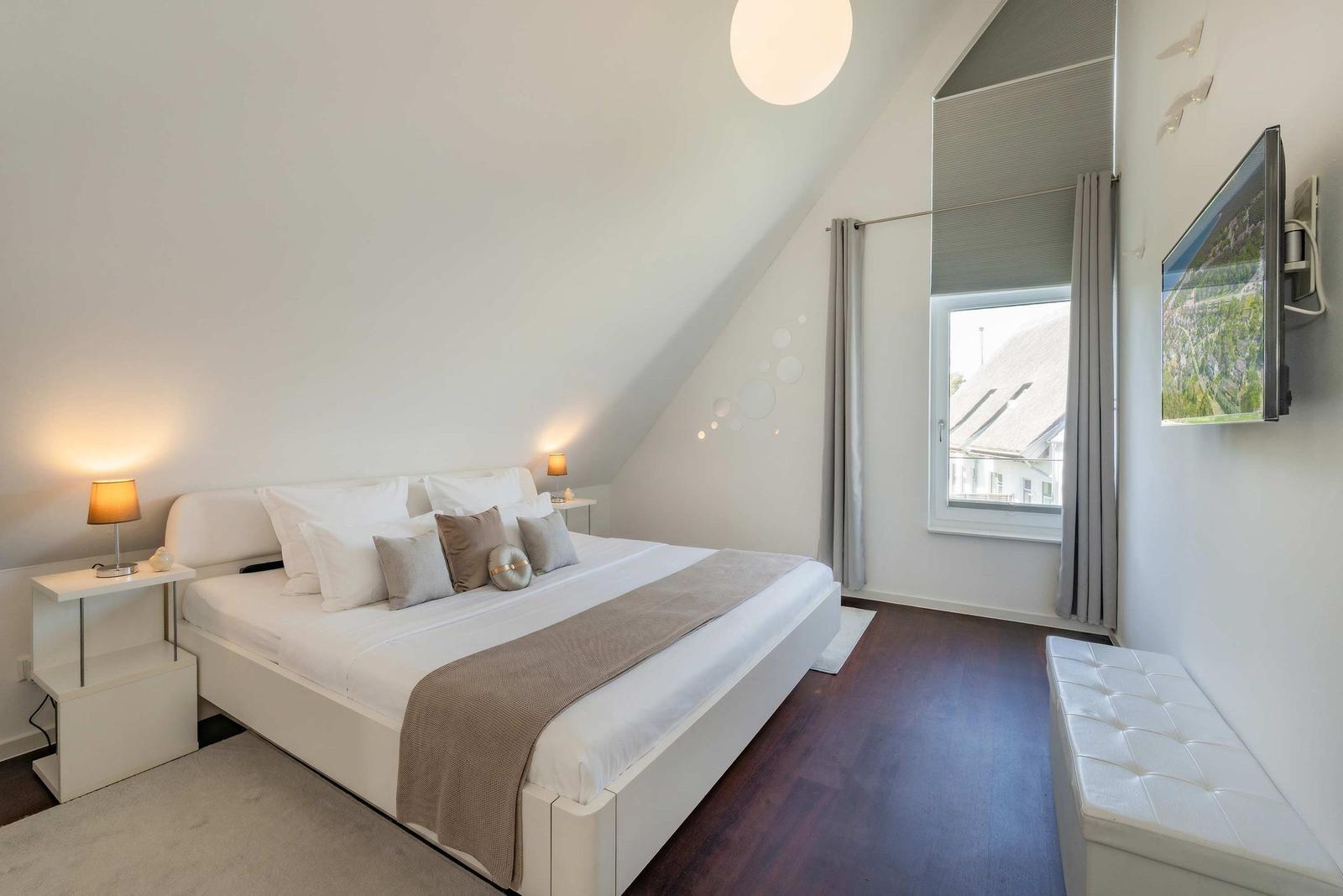 Schlafzimmer mit Dachschrägen, Bett, Nachttisch, Fenster und Wand-TV.