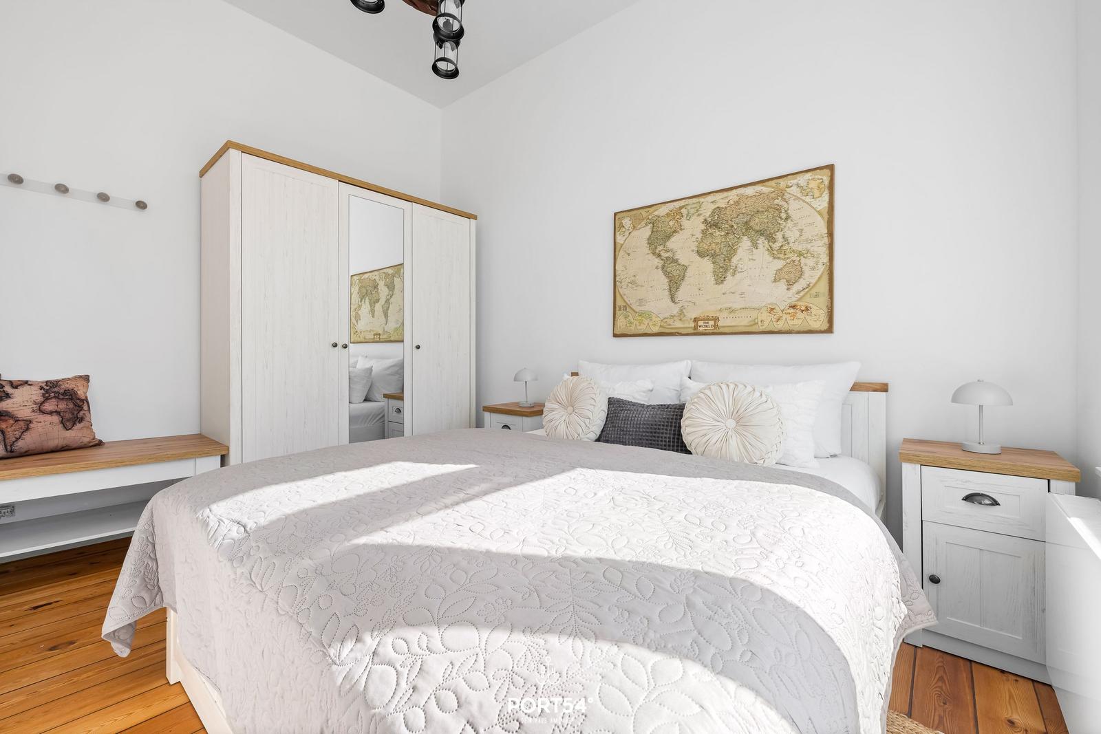 Schlafzimmer mit Bett, Kleiderschrank und Weltkarte an der Wand.