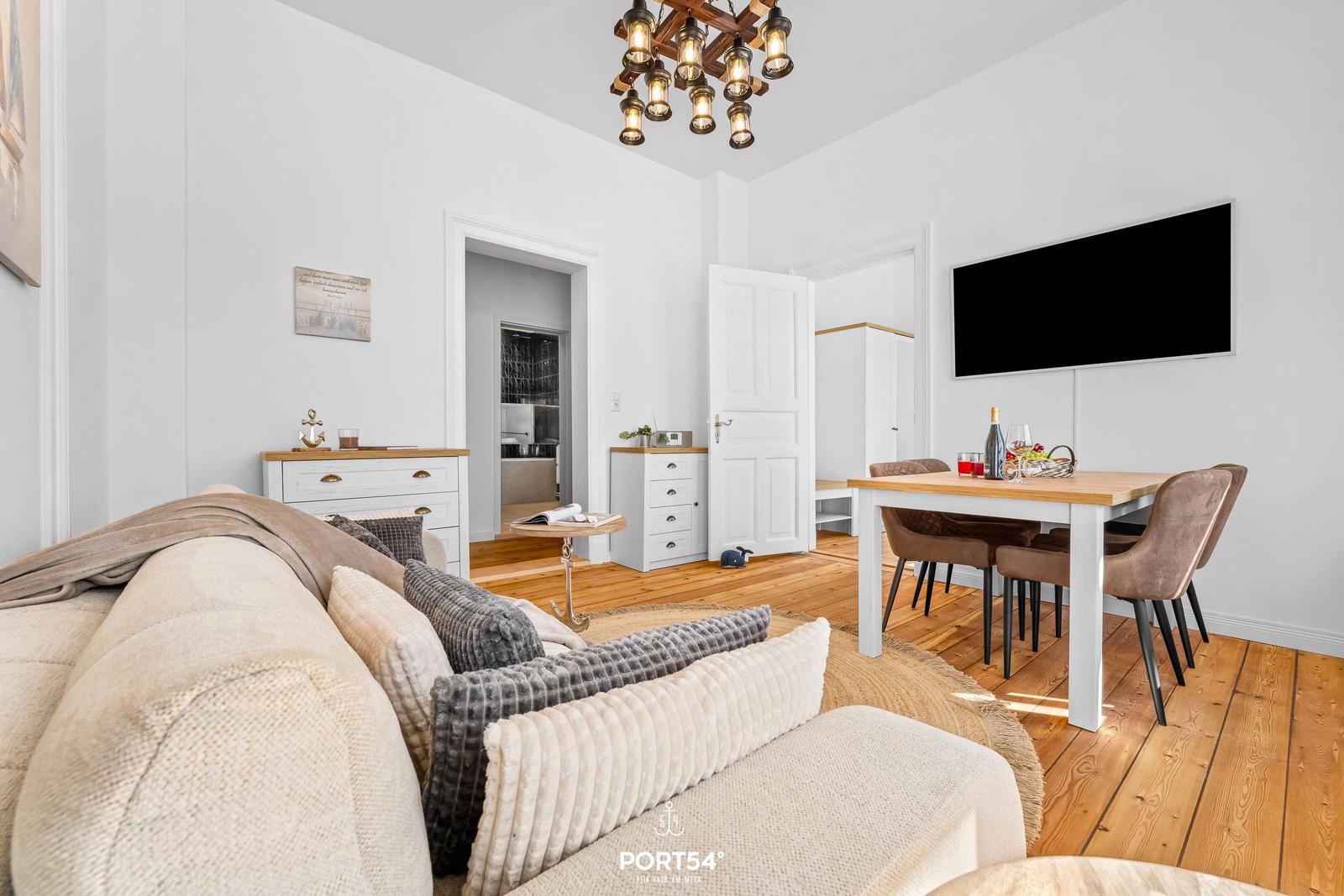 Wohn- und Essbereich mit Sofa, Esstisch und Fernseher an der Wand.