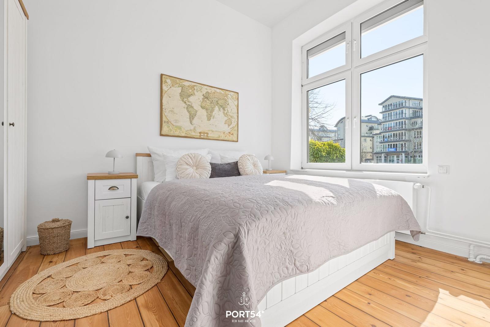 Schlafzimmer mit Bett, Nachttisch und Fensterblick auf Gebäude.