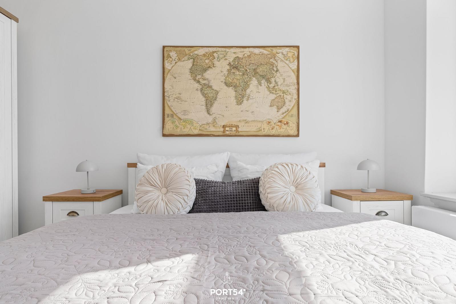 Schlafzimmer mit Bett, Nachttischen und Weltkarte an der Wand.