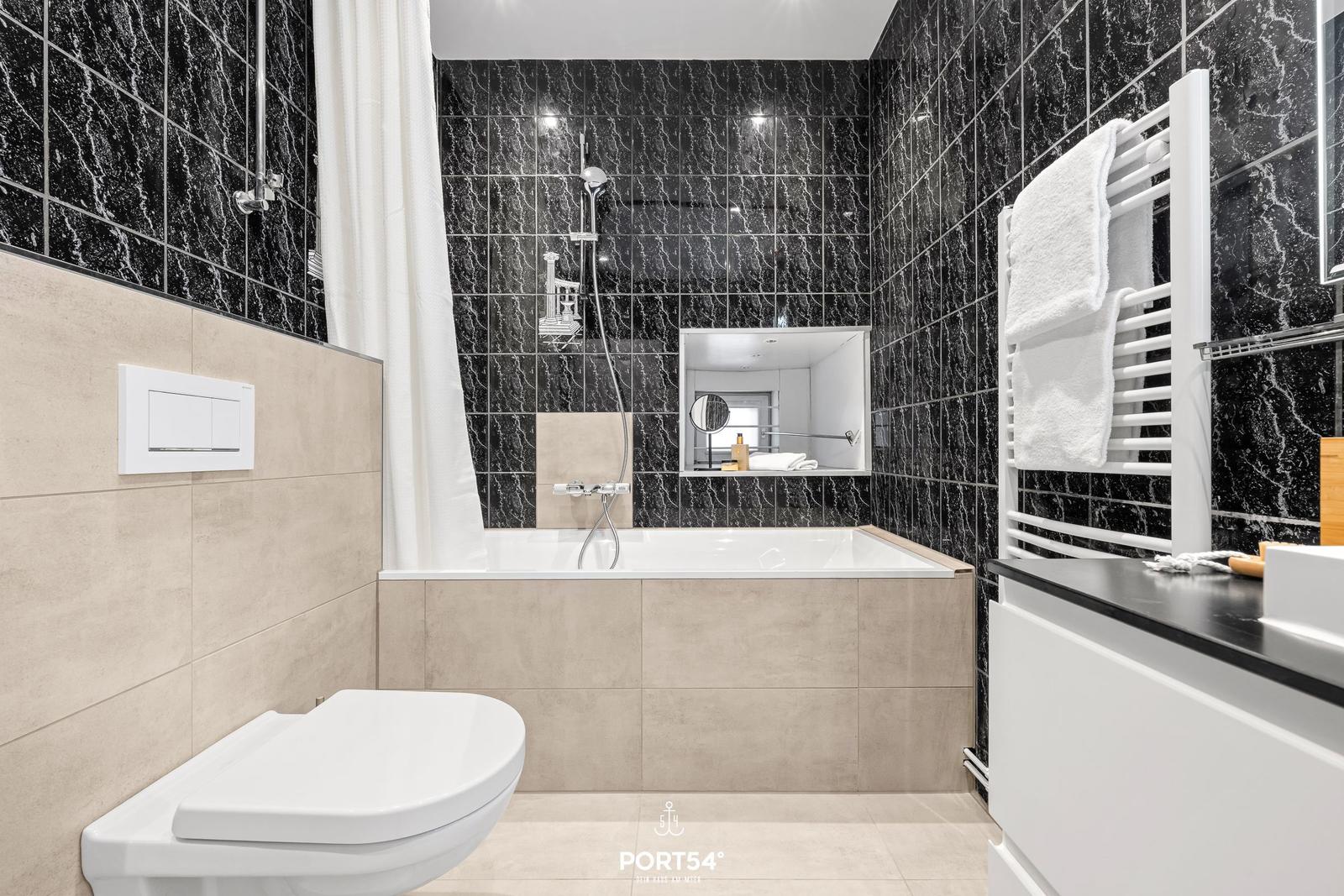 Badezimmer mit Badewanne, Dusche und Toilette. Schwarze Marmorfliesen und weiße sanitäre Einrichtung.