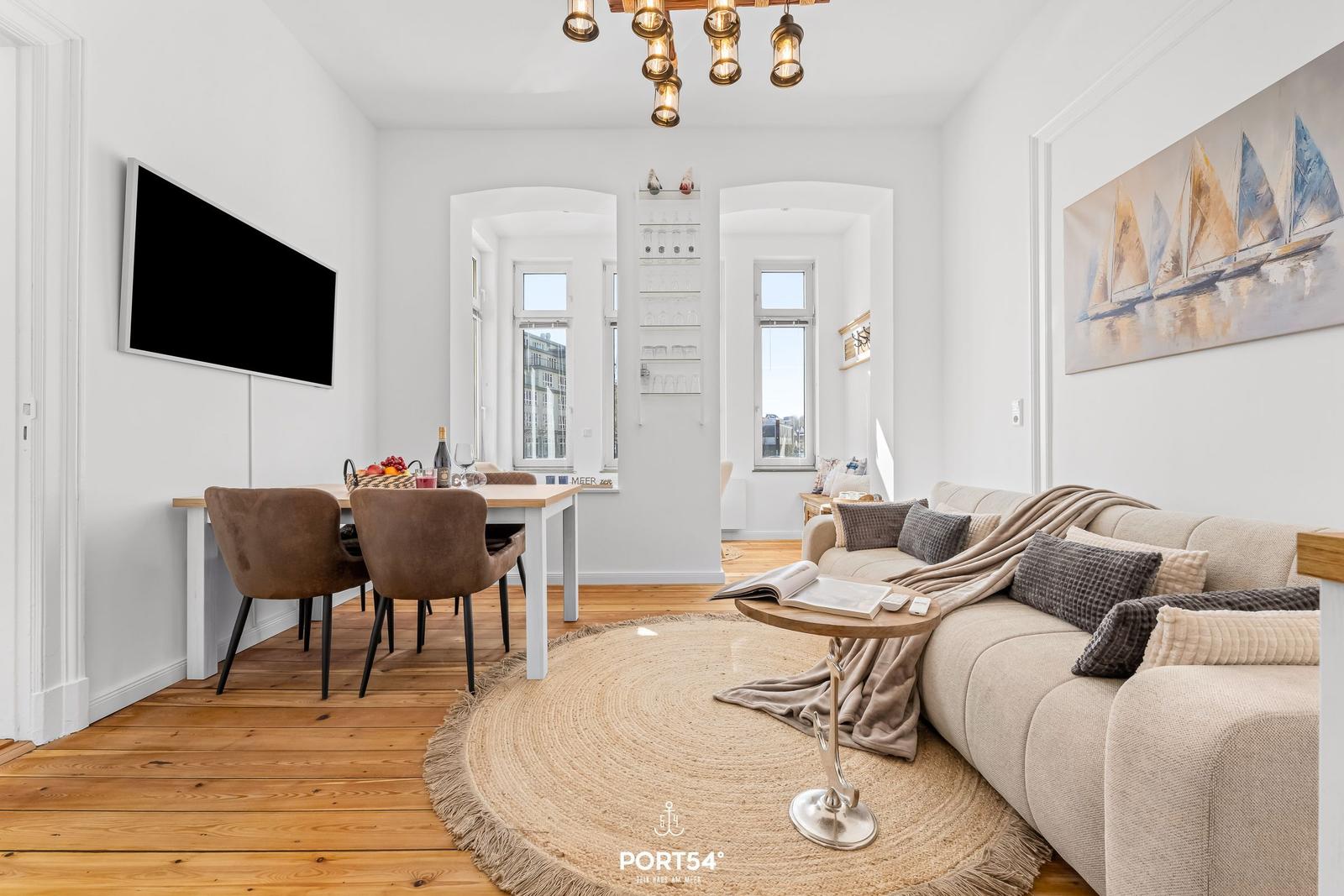 Wohn- und Essbereich mit Sofa, Esstisch und Wandbild mit Segelbooten.