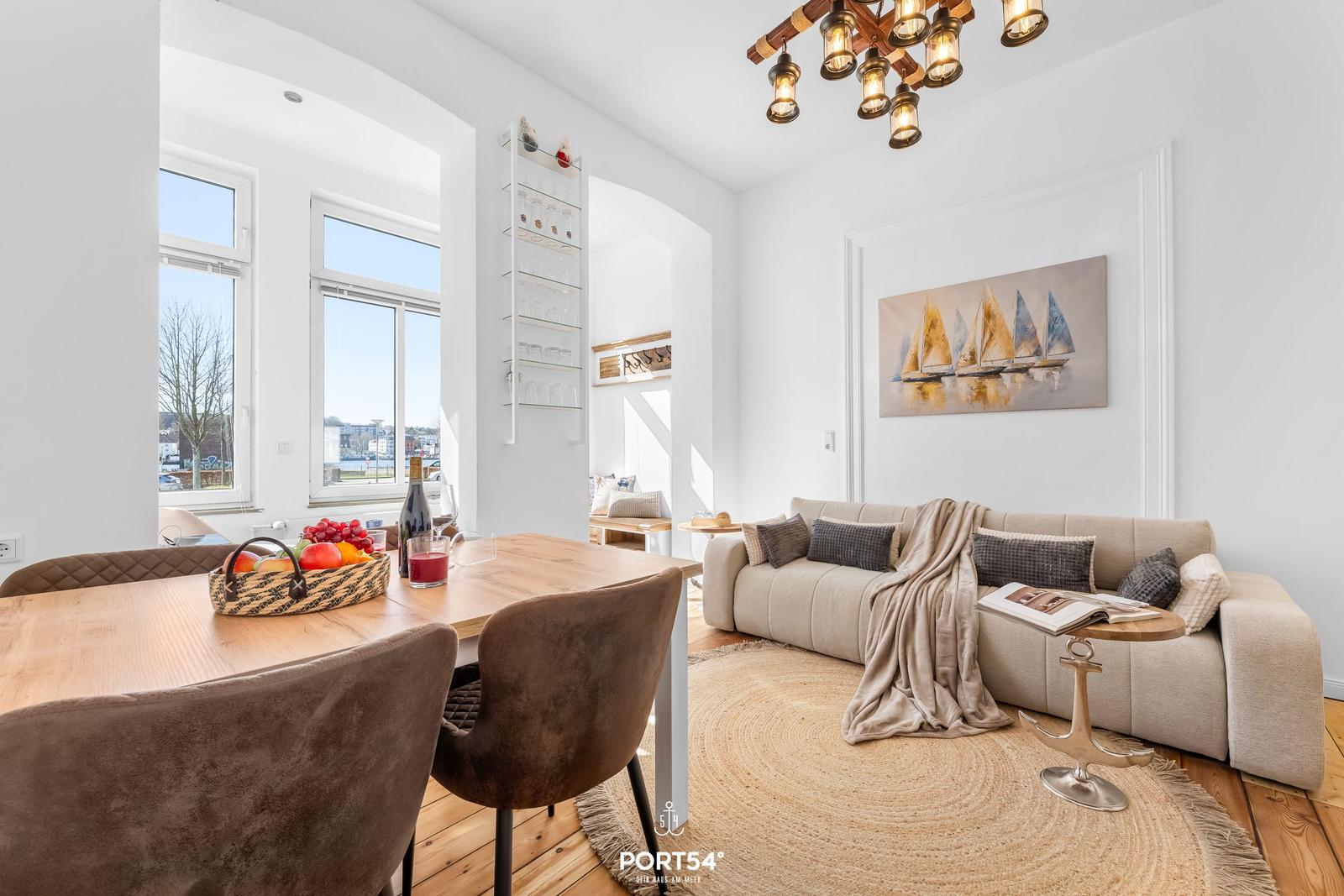 Essbereich mit Tisch und Stühlen, Wohnbereich mit Sofa und Wandbild.