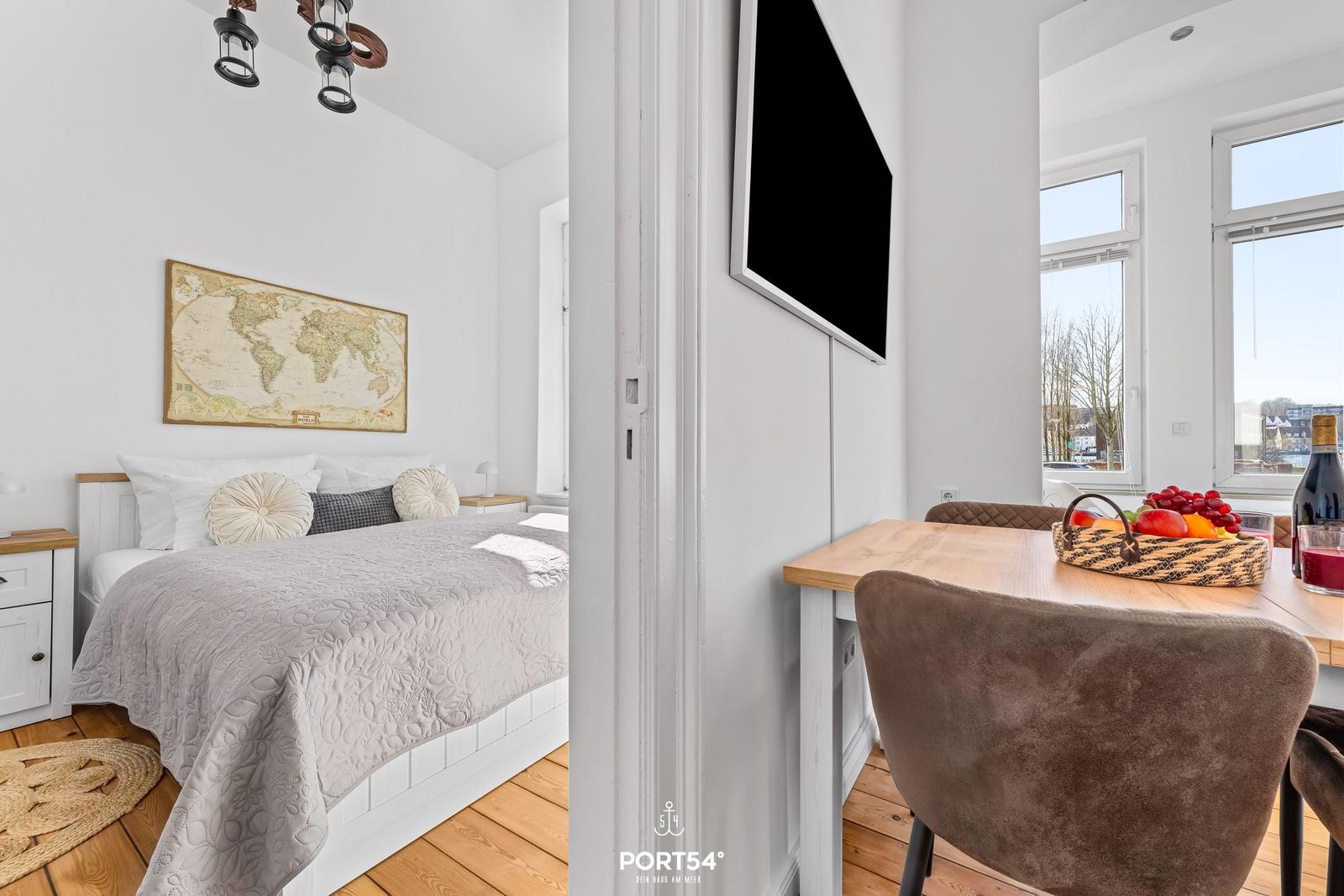 Schlafzimmer mit Bett und Weltkarte. Nebenraum mit Esstisch und TV.