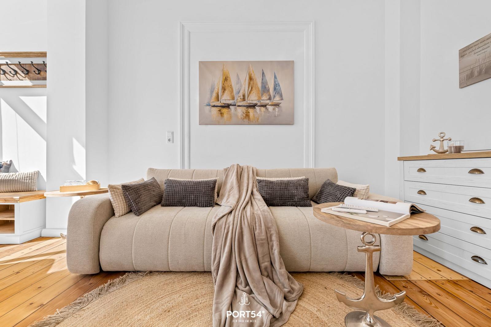 Ein Wohnzimmer mit Sofa, Kissen, Decke und Wandbild mit Segelbooten.